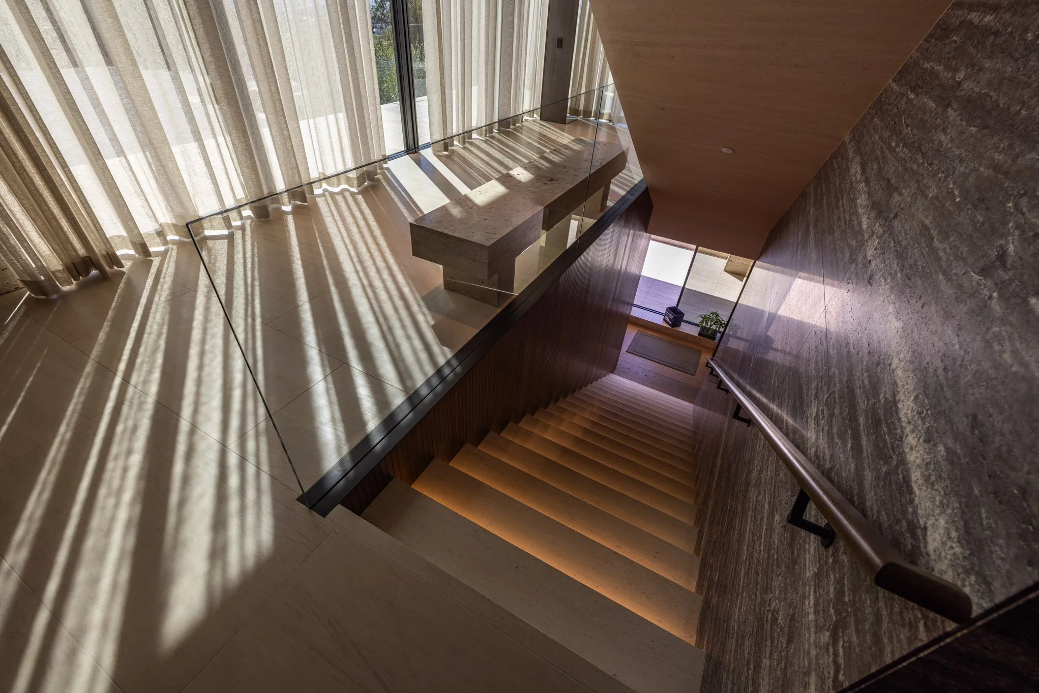 Interior view of a modern staircase with wooden steps and illuminated by natural light through large windows with curtains.