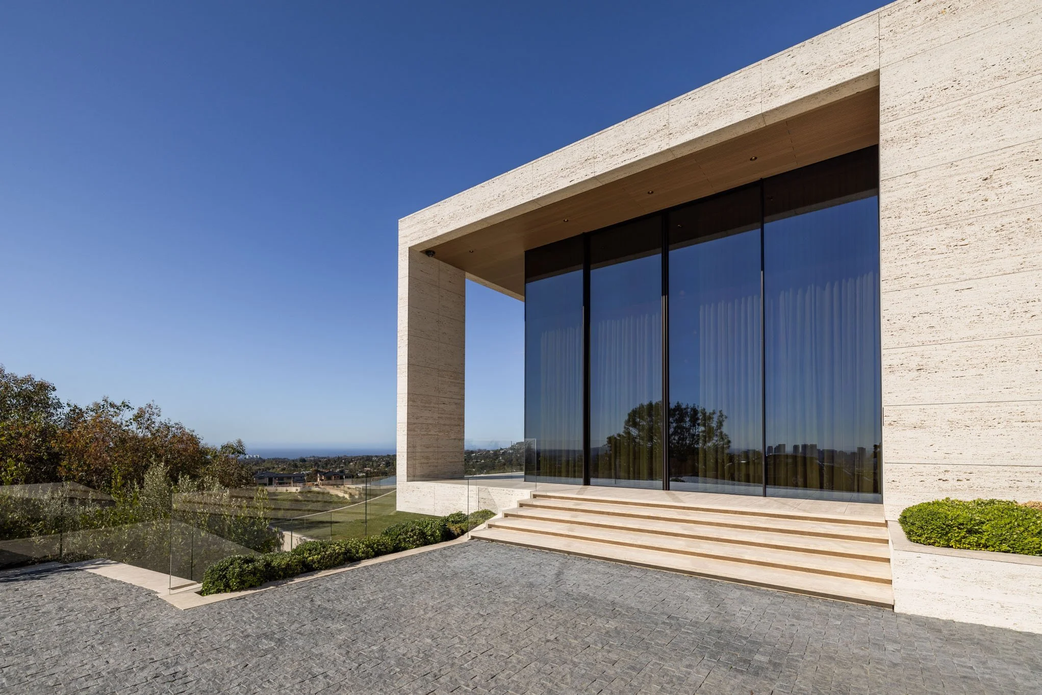 Modern building with large glass doors, stone exterior, steps leading to entrance, and a clear blue sky