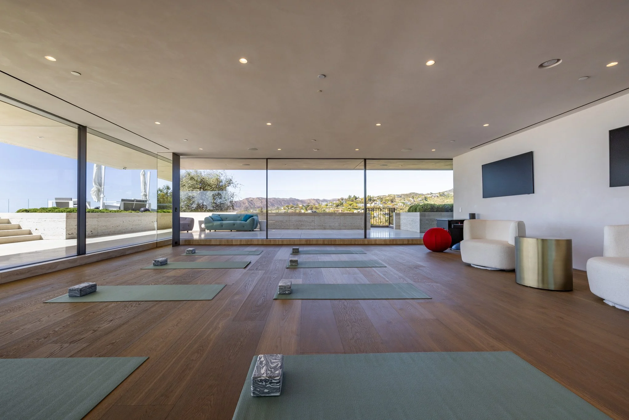 Modern yoga studio with large windows, light hardwood floors, yoga mats and blocks laid out, and scenic mountain view outside.