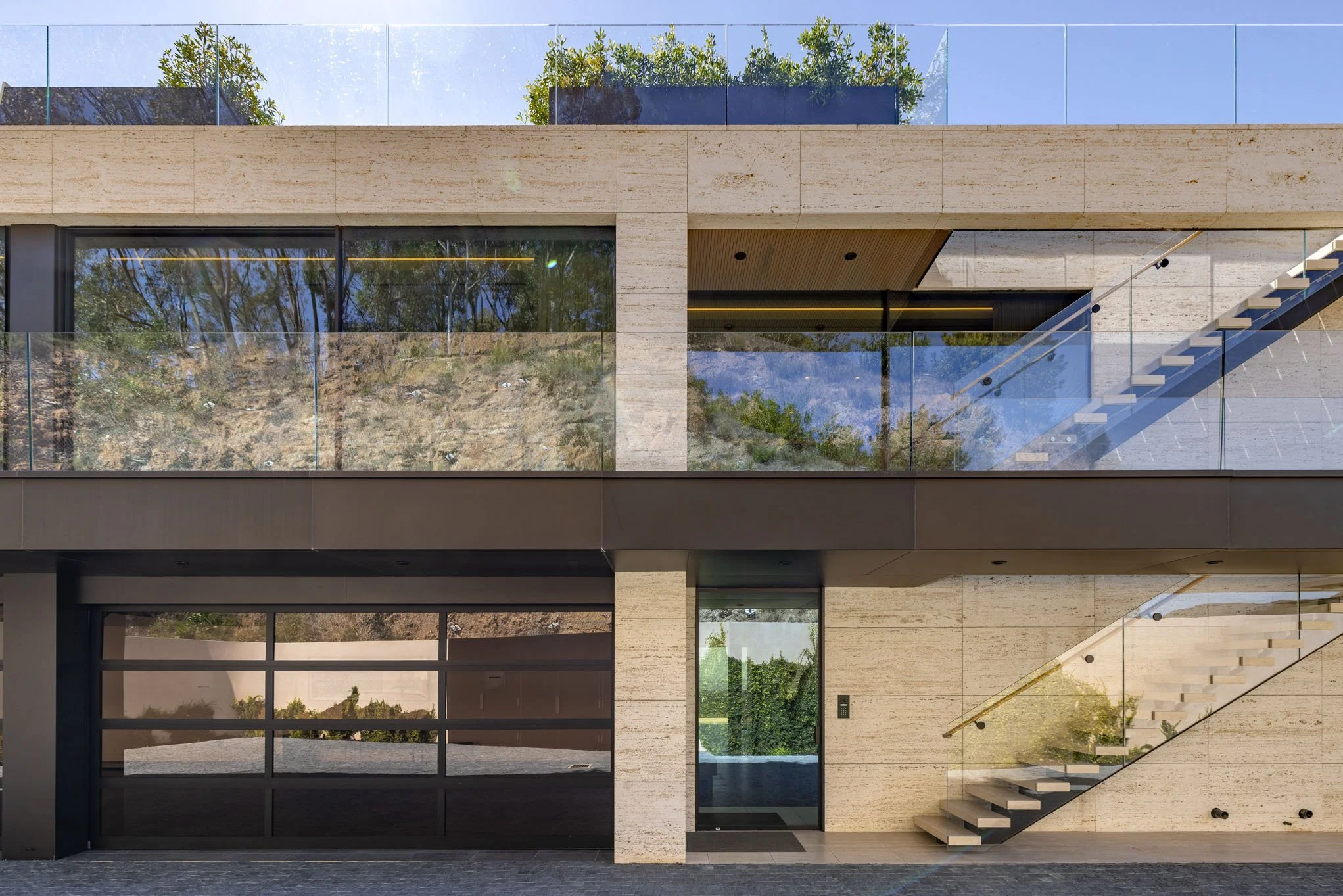 Modern multi-story building with large glass windows, outdoor stairs, and a rooftop garden visible through the glass railing.