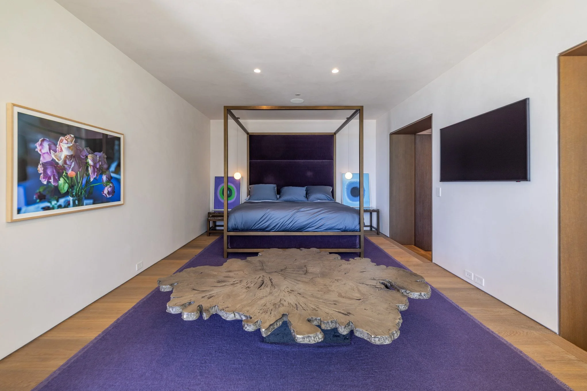 Modern bedroom with purple canopy bed, abstract artwork, wooden floor, and sliding door.
