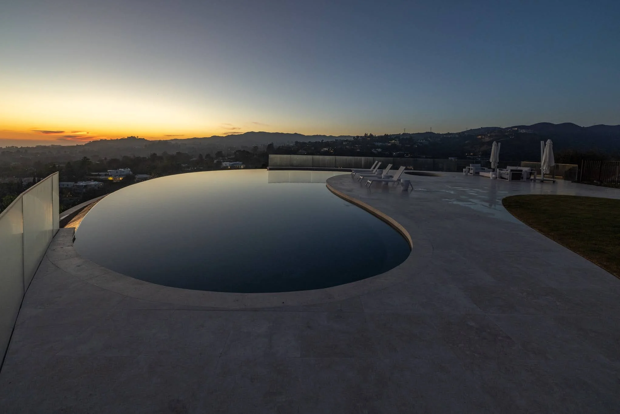 Infinity swimming pool on a rooftop terrace at sunset with lounge chairs and umbrellas in the background.