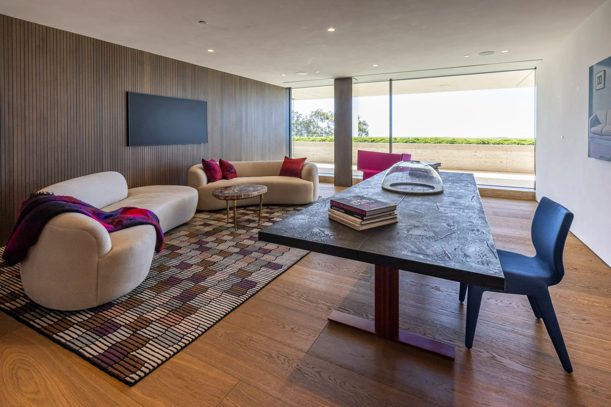 Modern living room with two white sofas, a colorful patterned rug, a rectangular coffee table, and a large window with a view of green landscape