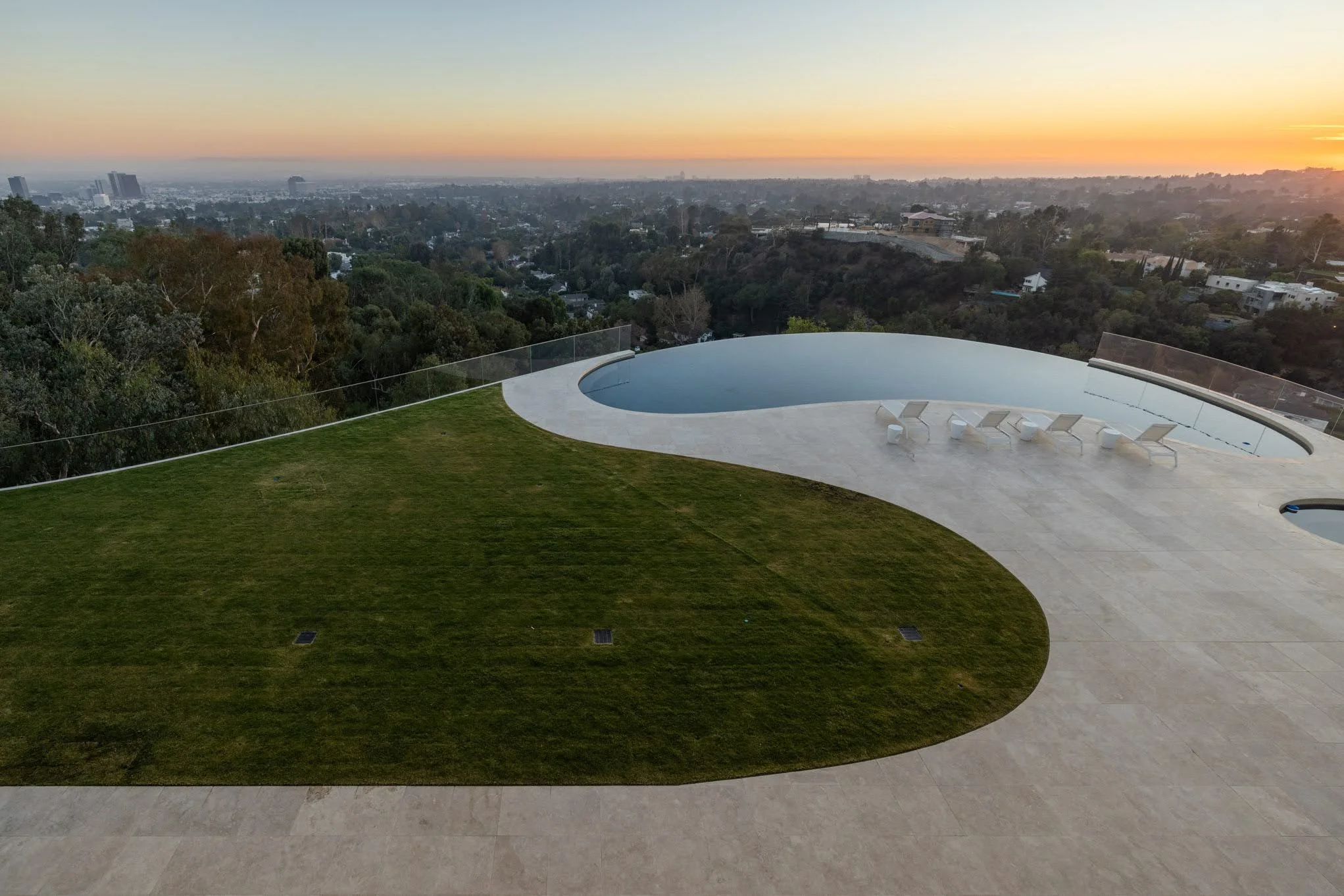 Rooftop pool with lounge chairs overlooking a cityscape at sunset
