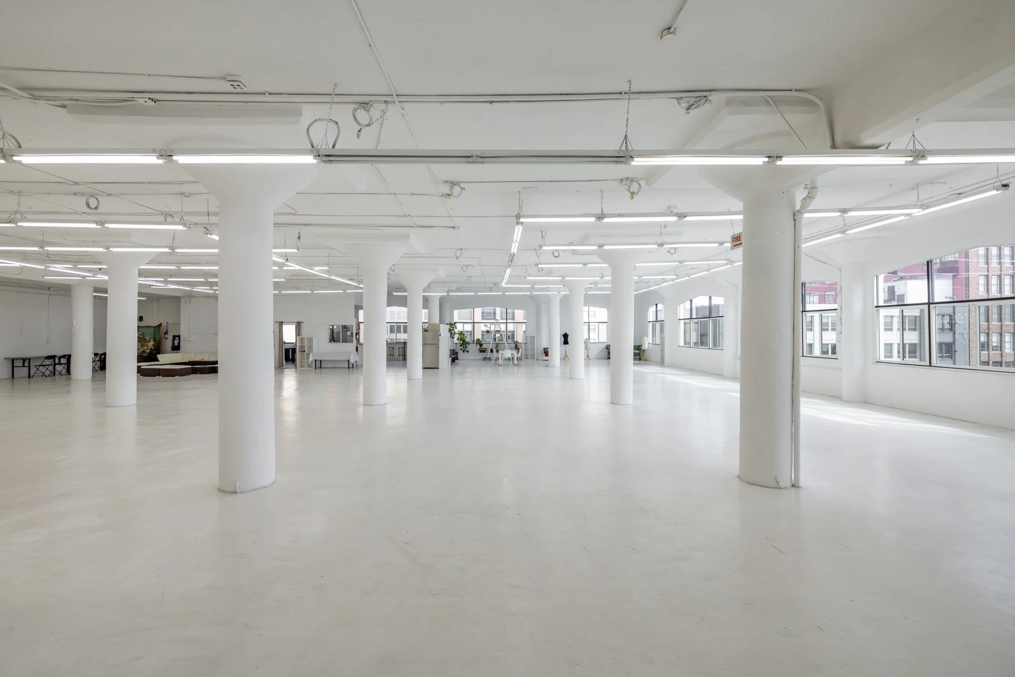 Spacious, empty white-walled room with large windows, white columns, and ceiling lights.
