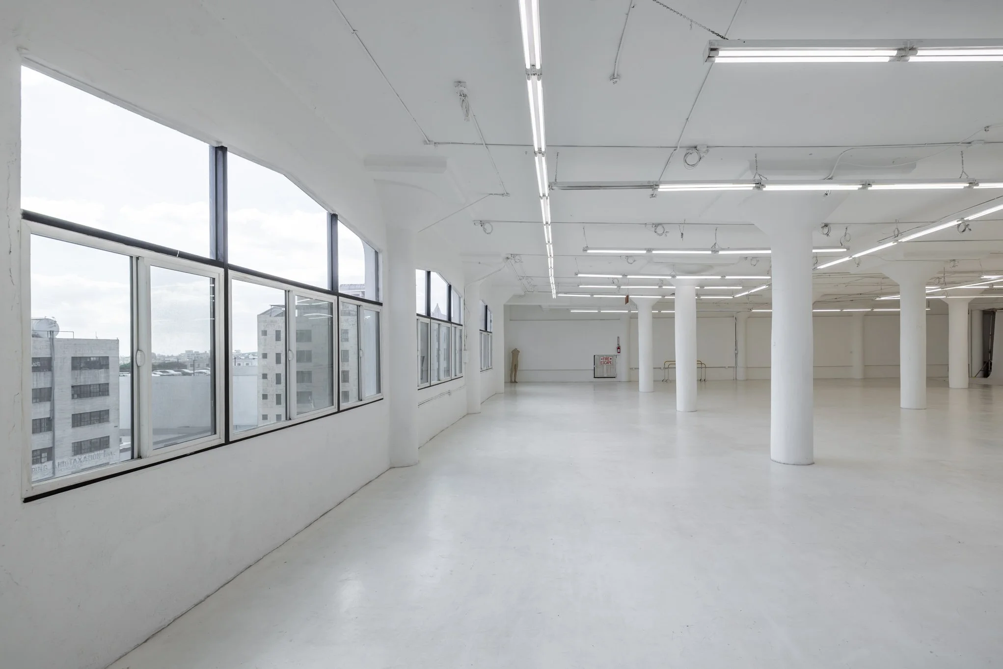 Empty white commercial or studio space with large windows, white walls, and ceiling lights.