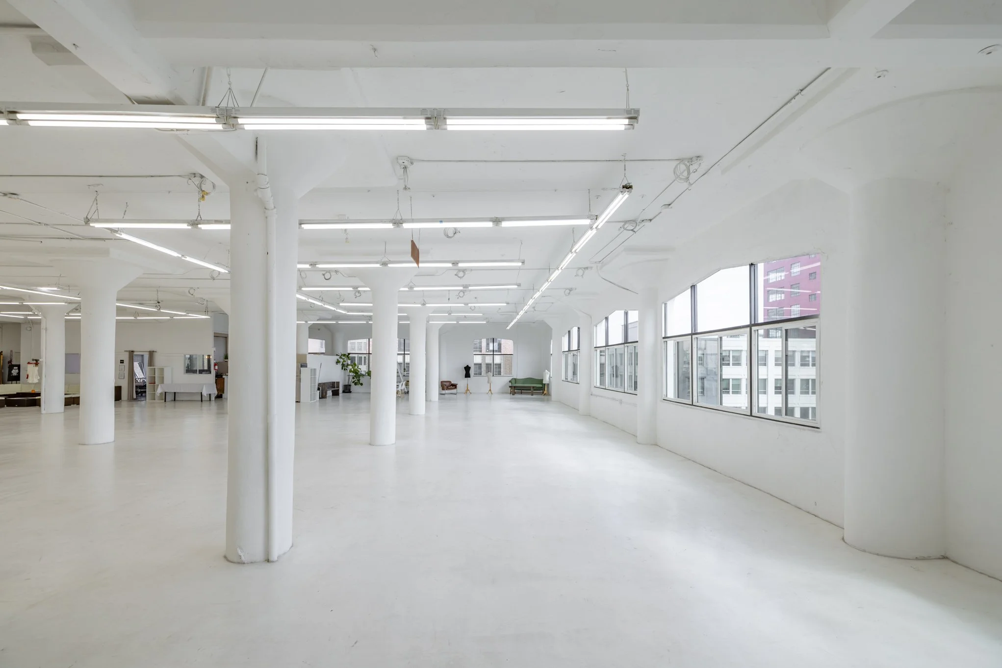 Empty white industrial-style room with large windows and hanging fluorescent lights.
