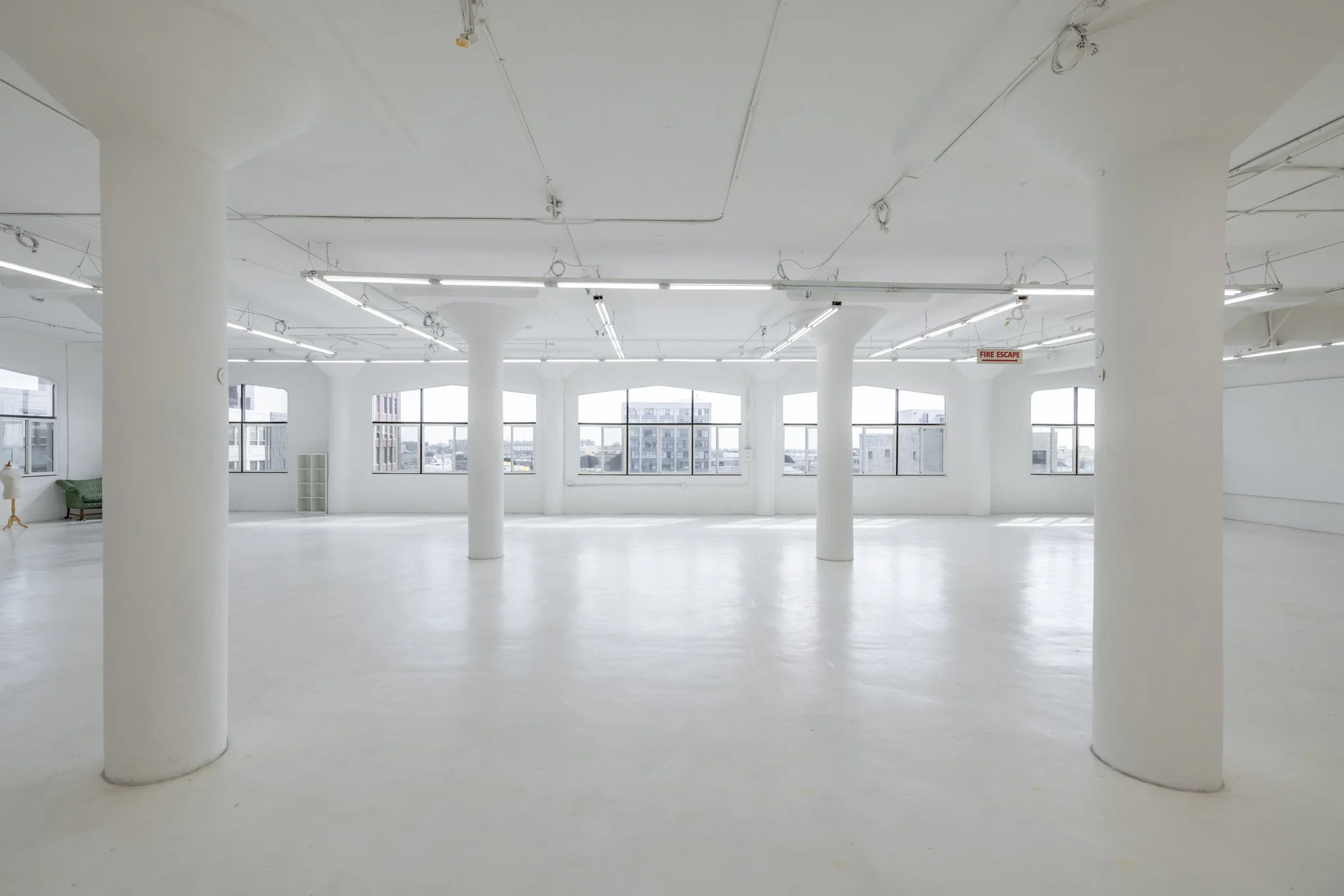 Empty, white, spacious room with large windows, white columns, and ceiling lights.