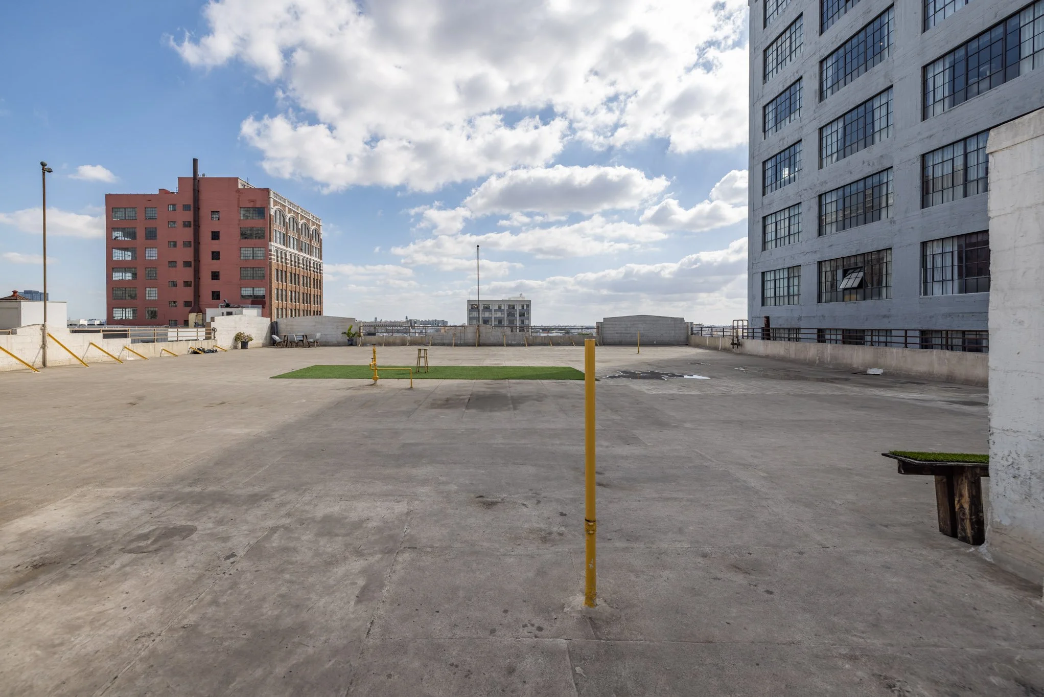 Rooftop parking lot with a small grassy area, surrounded by tall buildings and a partly cloudy sky.