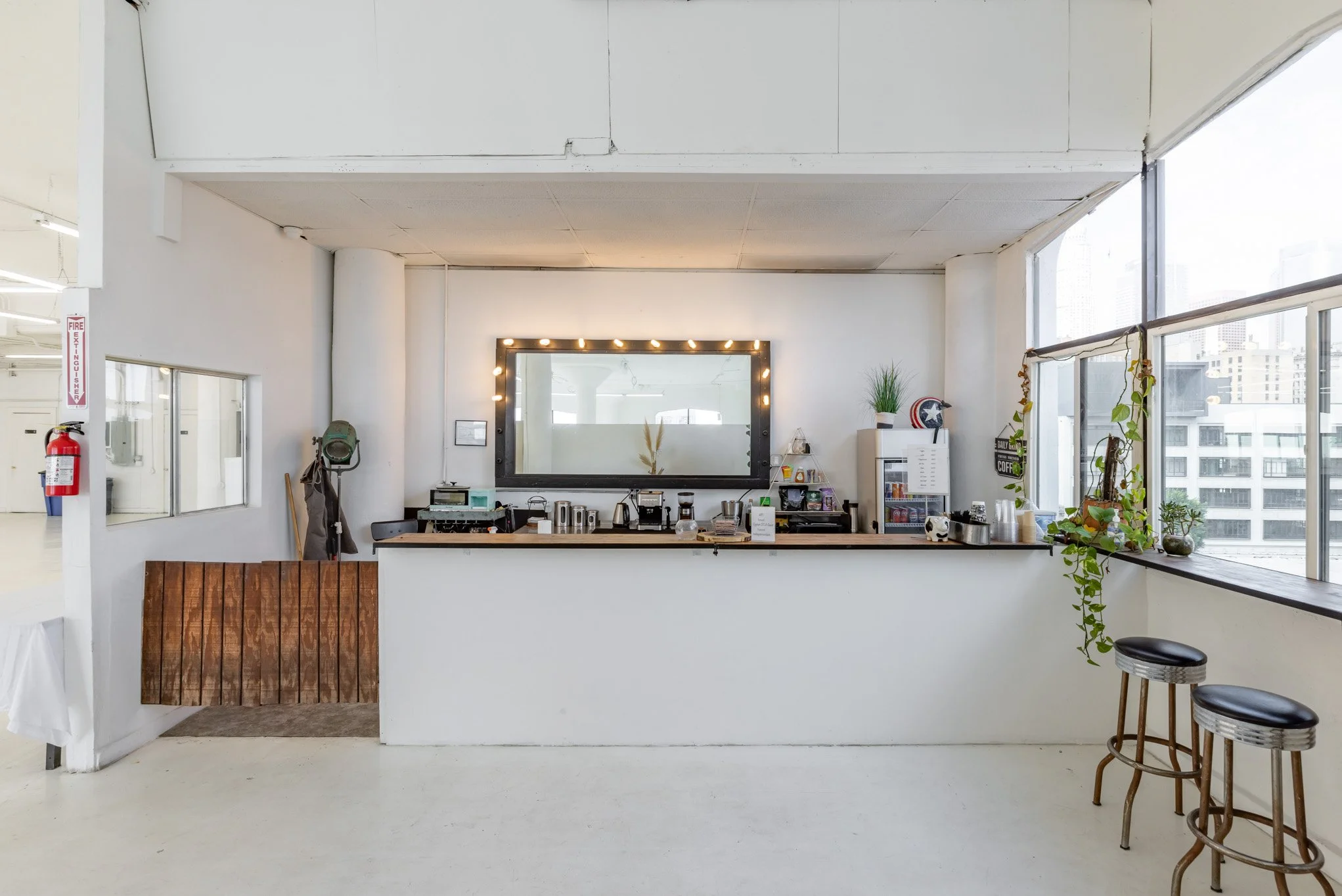 Coffee bar with a large mirror, plants, and stools by the window in a bright, modern space