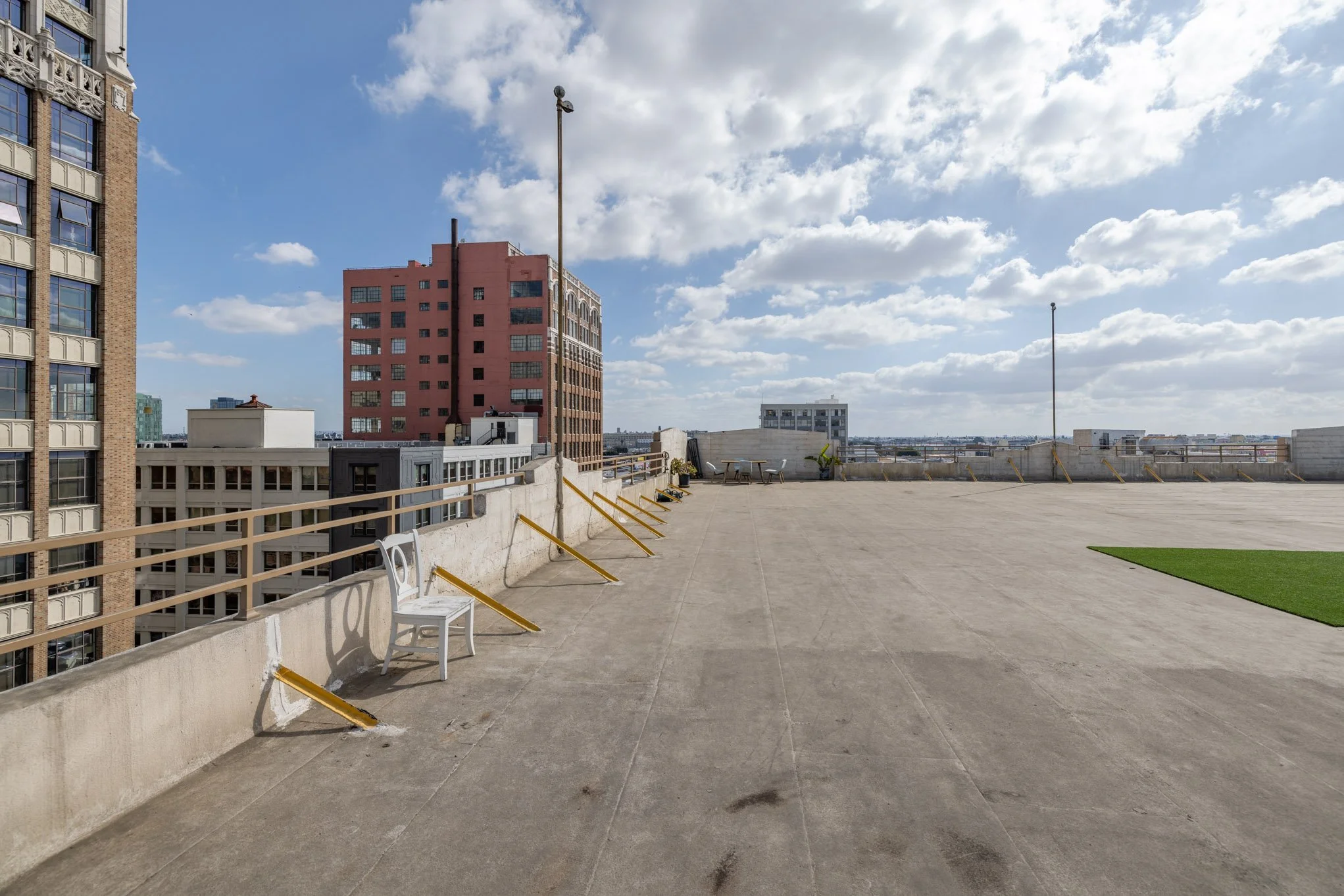 Empty rooftop parking lot with a white chair, rooftop cityscape view of tall buildings, partly cloudy sky