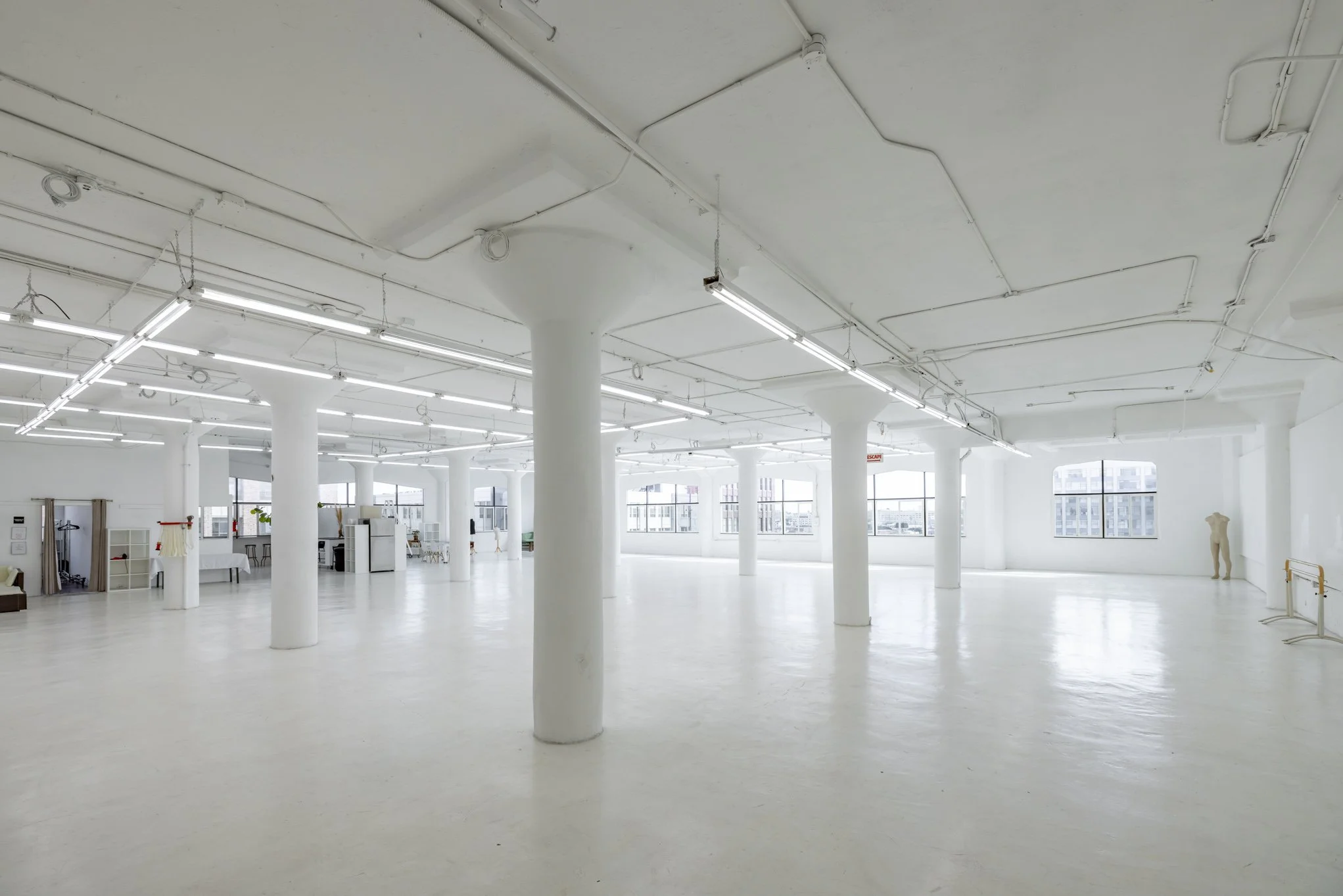 Spacious, empty, white studio or gallery with large windows and cylindrical support columns.
