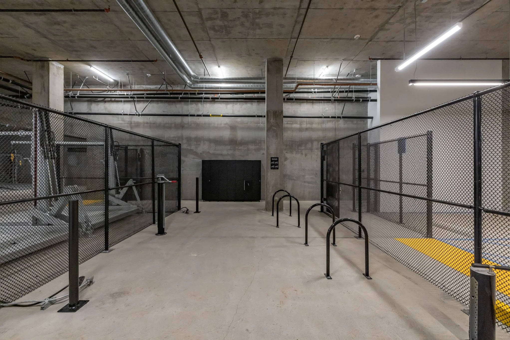 Underground parking garage with concrete floors and walls, black metal bike racks, and fencing on both sides.