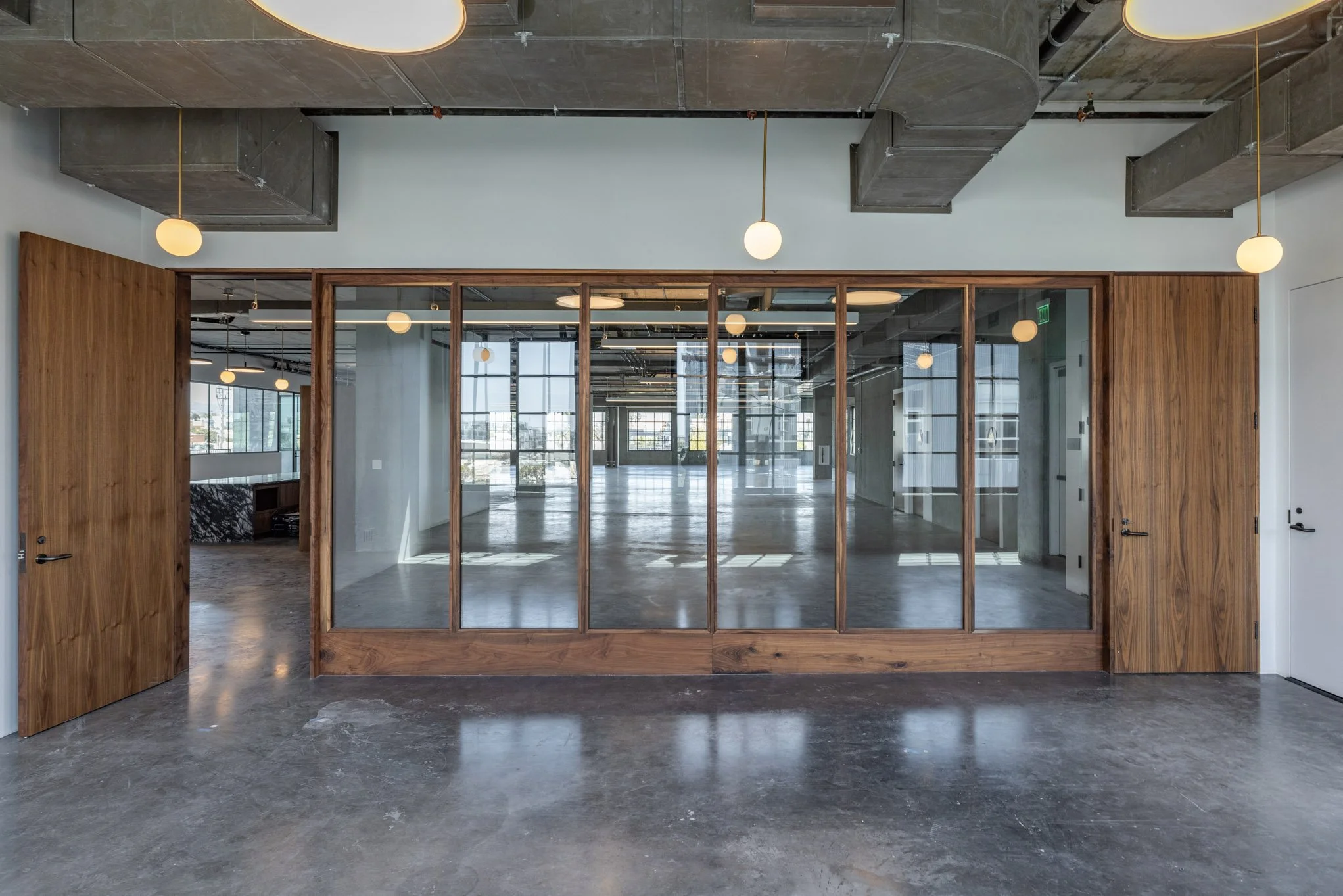 Modern office interior with glass walls, wooden doors, and hanging round light fixtures, empty space with large windows.