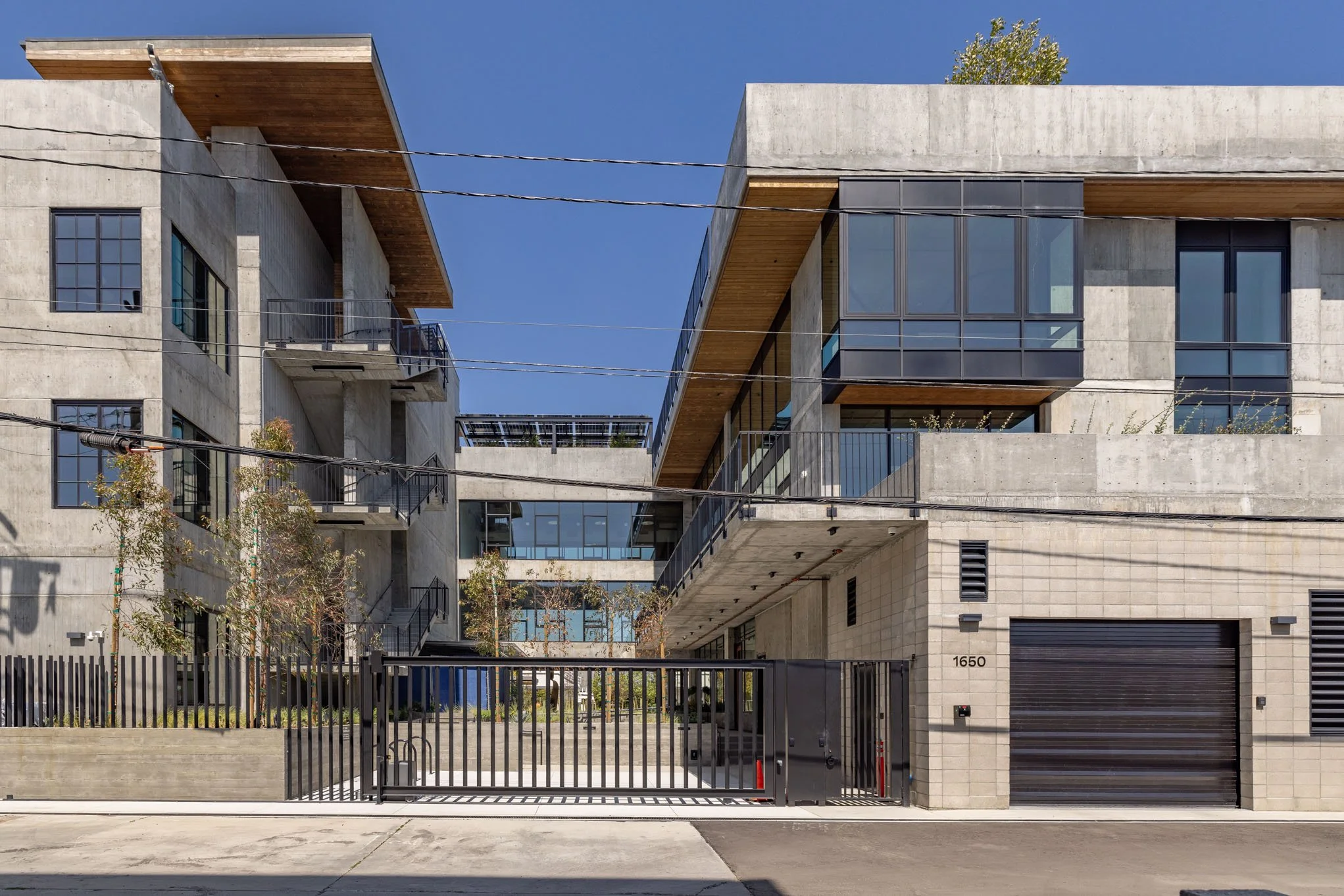 Modern multi-story apartment building with concrete and glass facade, balconies, and a gated entrance with the number 1650.