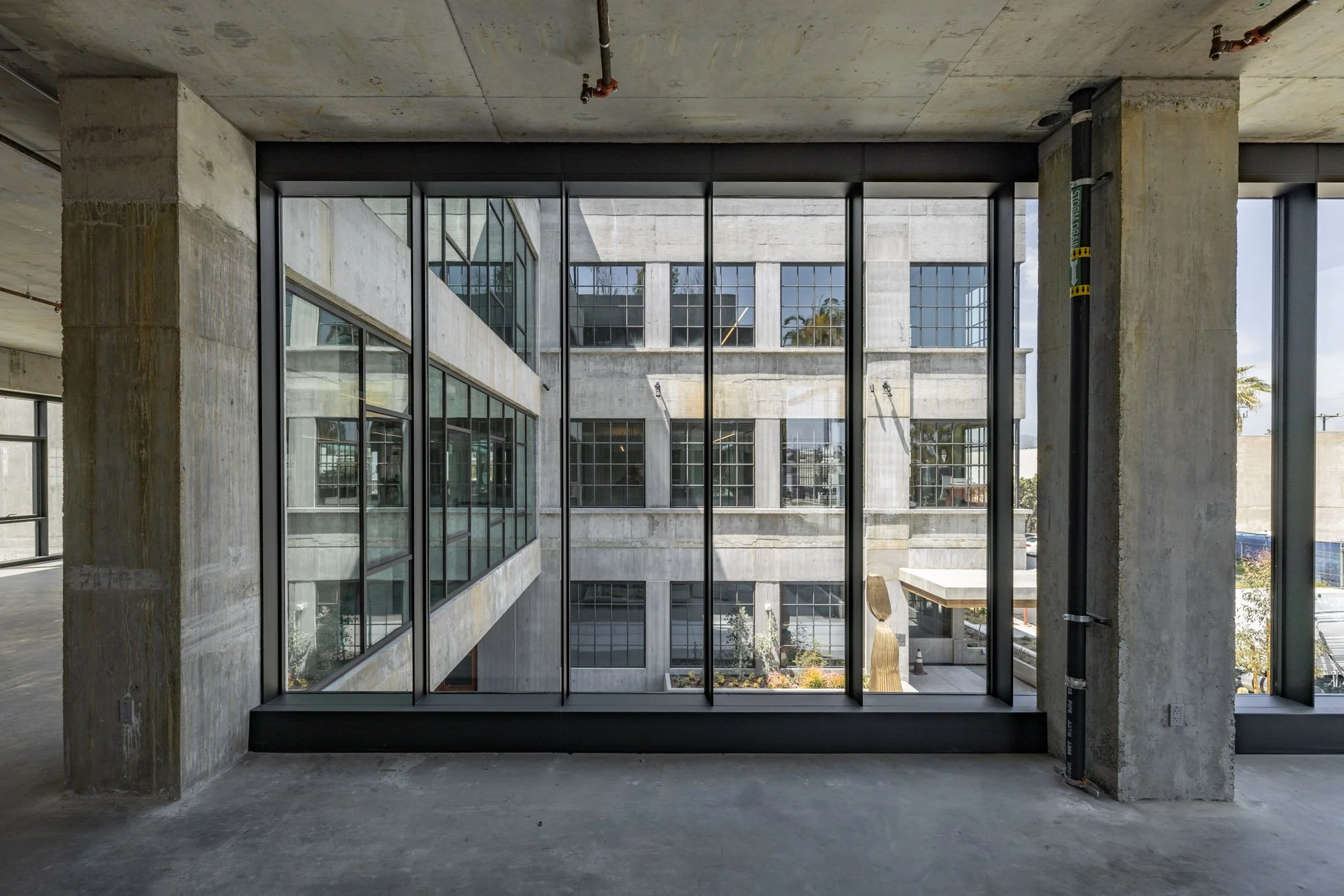 Interior of an unfinished building with exposed concrete walls and floor, large glass window panes, and urban view outside.