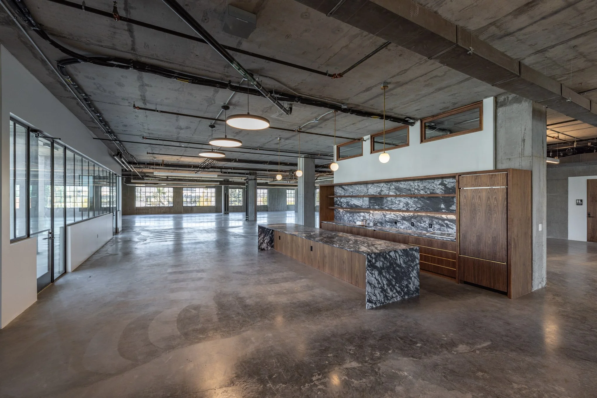 Empty modern commercial interior with polished concrete floors, exposed ceiling, a marble counter with a wooden base, and large windows