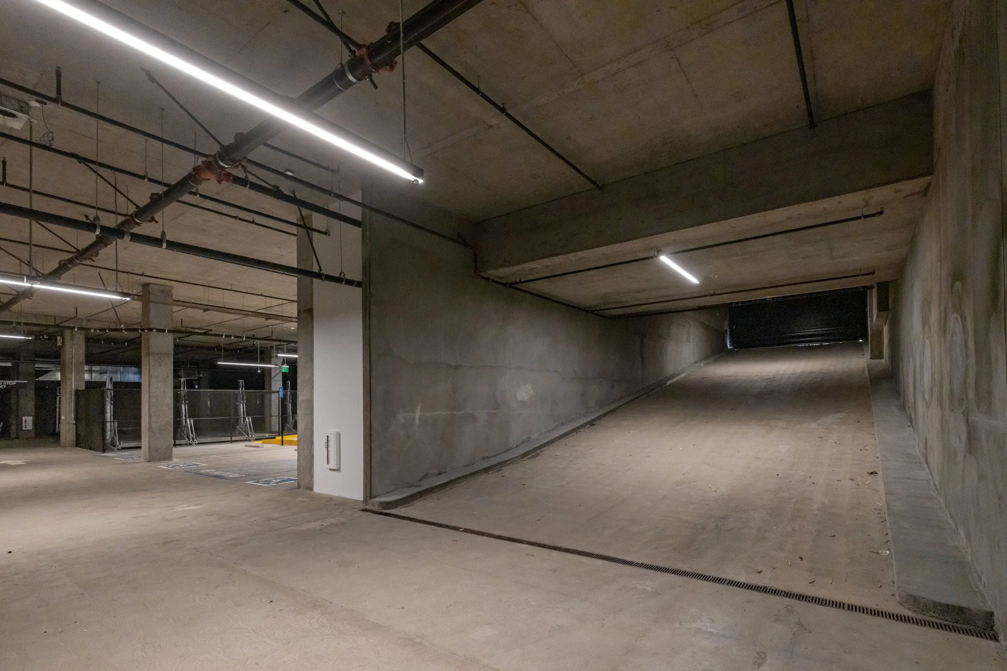 Underground parking garage with concrete pillars, ramps, and fluorescent lighting.