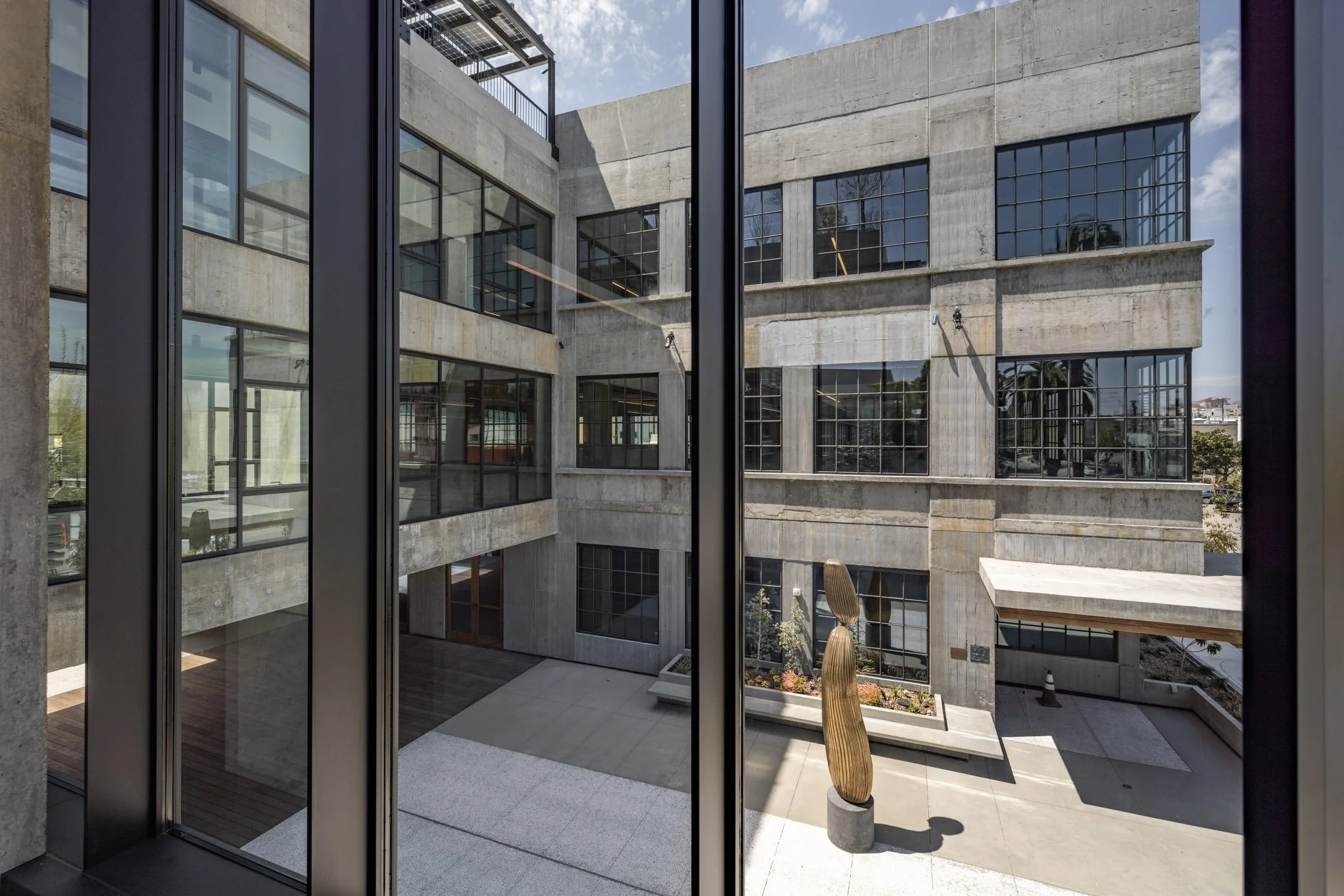 View of a modern concrete building with large glass windows and an outdoor courtyard with abstract sculptures.