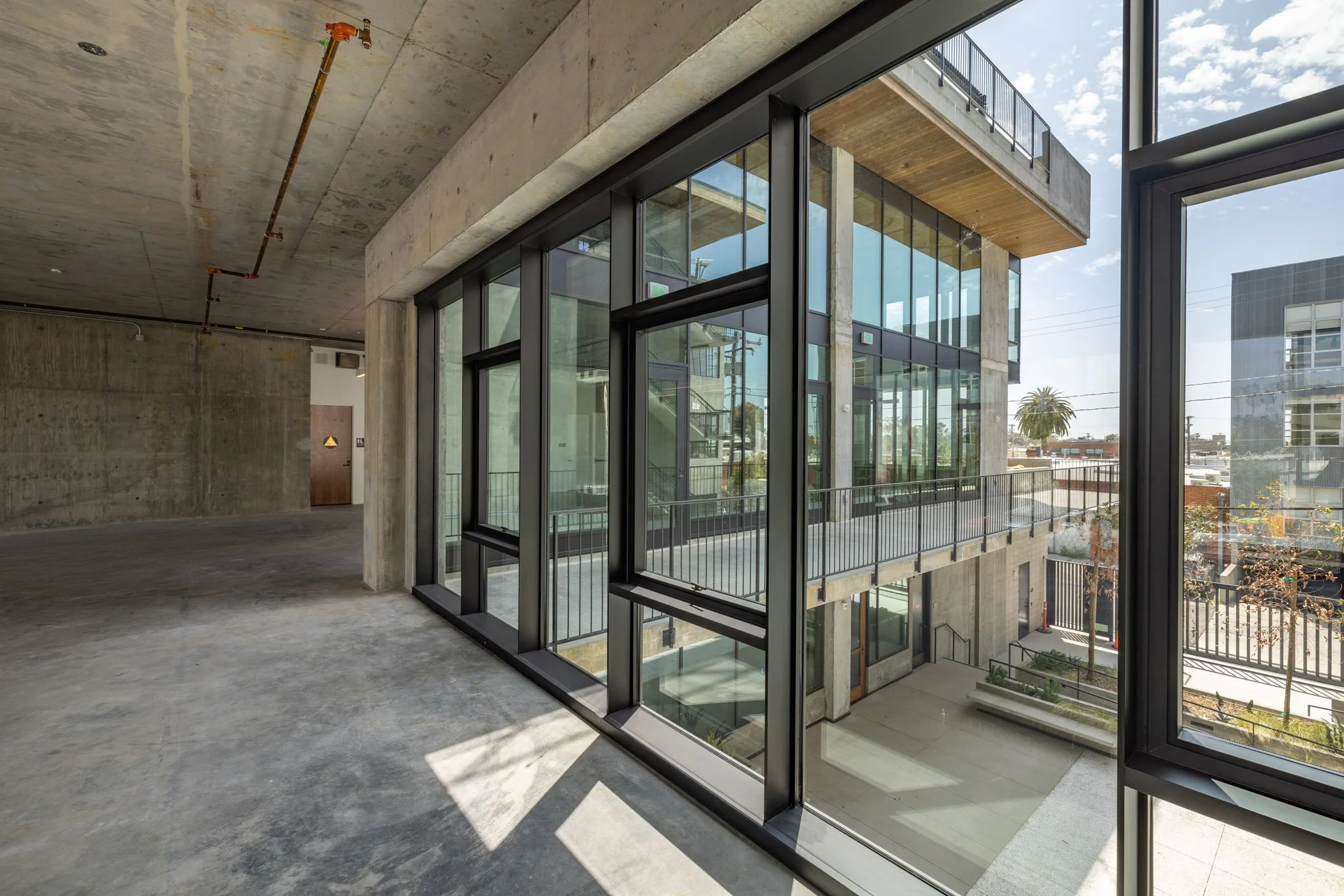 Interior view of a modern building with large glass windows, concrete walls, and an open space with visible shadows on the floor.
