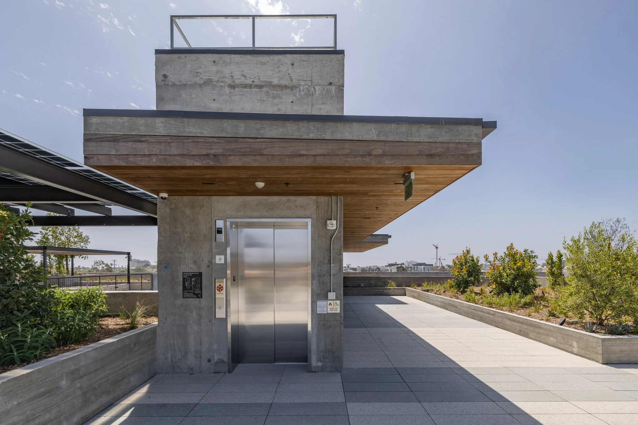 Modern rooftop view with an elevator, greenery, and a blue sky.