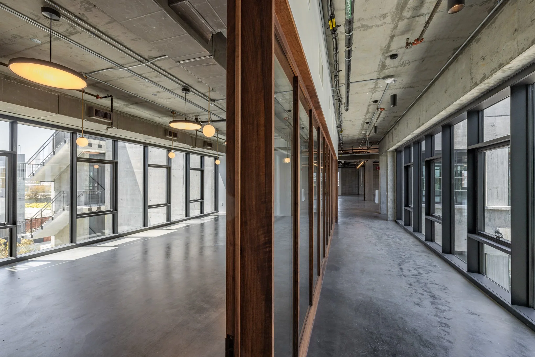Empty modern office space with large windows, concrete ceiling, and wooden partitions.