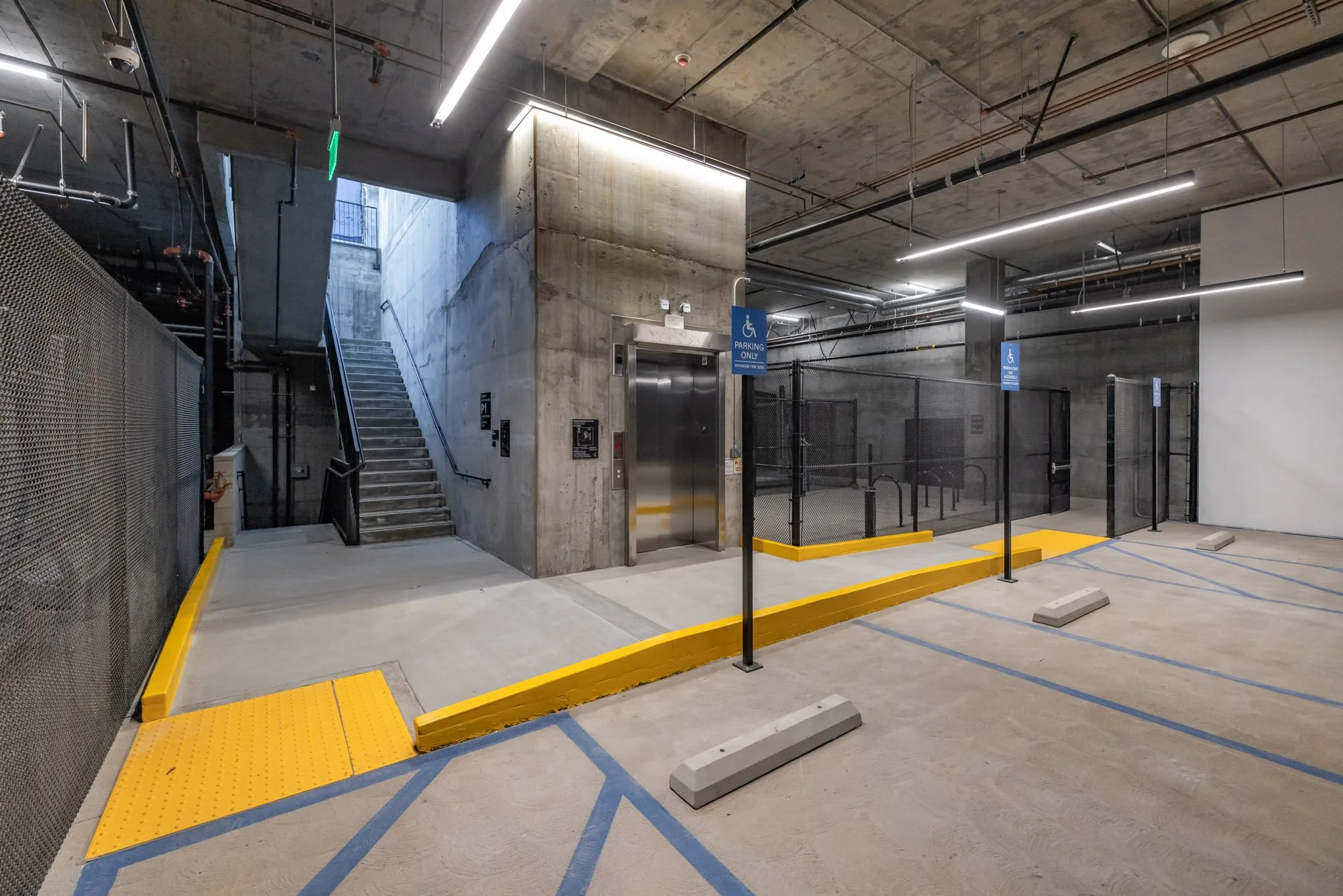 Underground parking garage with accessible elevator, staircase, designated disabled parking spots, and signs indicating parking for disabled individuals.