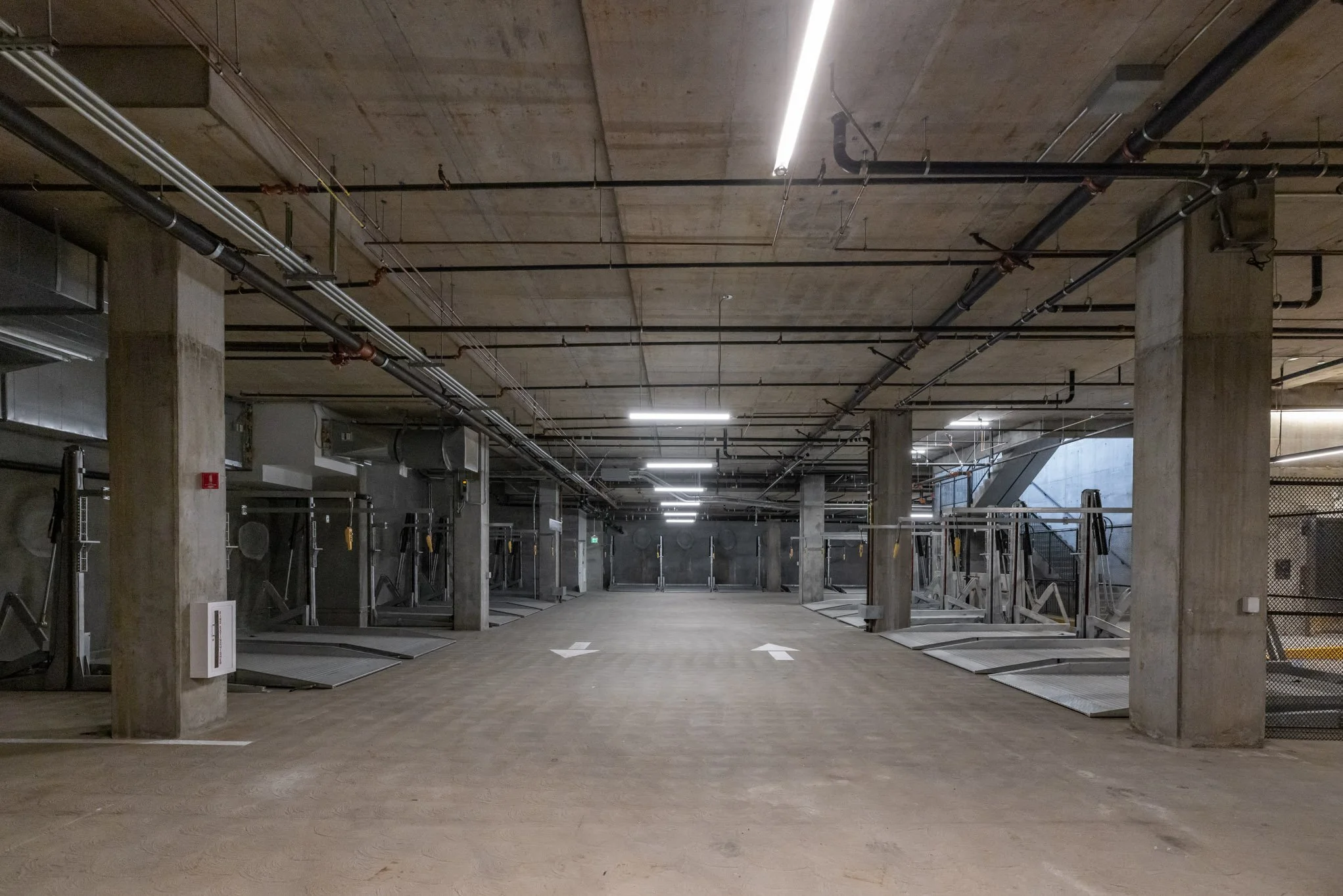 Underground parking garage with gym equipment on the sides and concrete pillars, lit by overhead fluorescent lights.