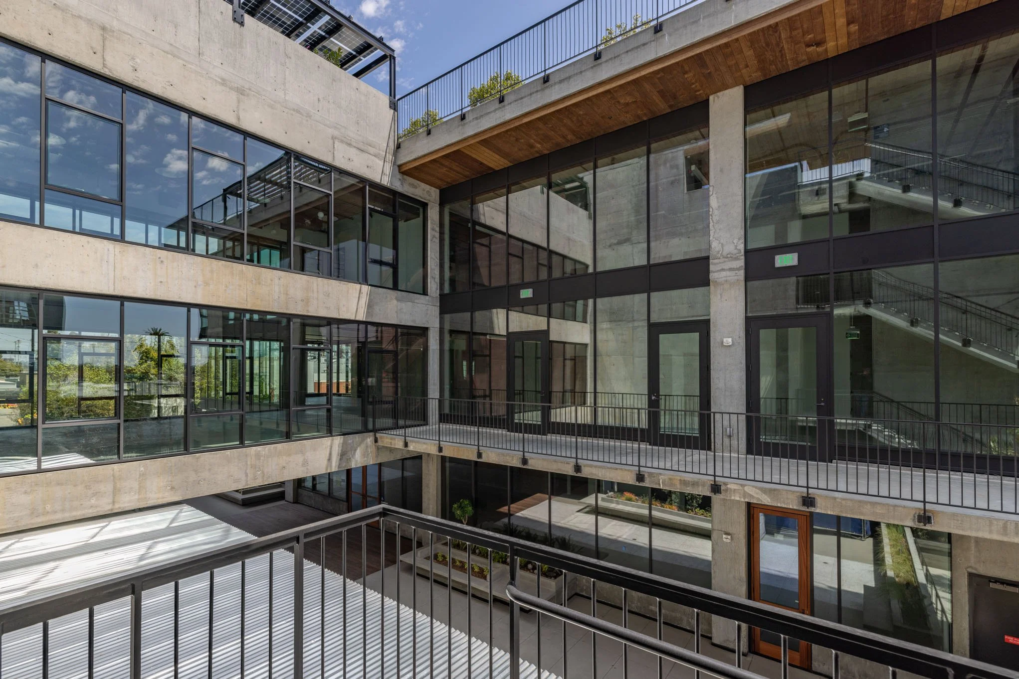 Modern multi-story office building with large glass windows and concrete walls, featuring outdoor walkways and staircases, under a blue sky