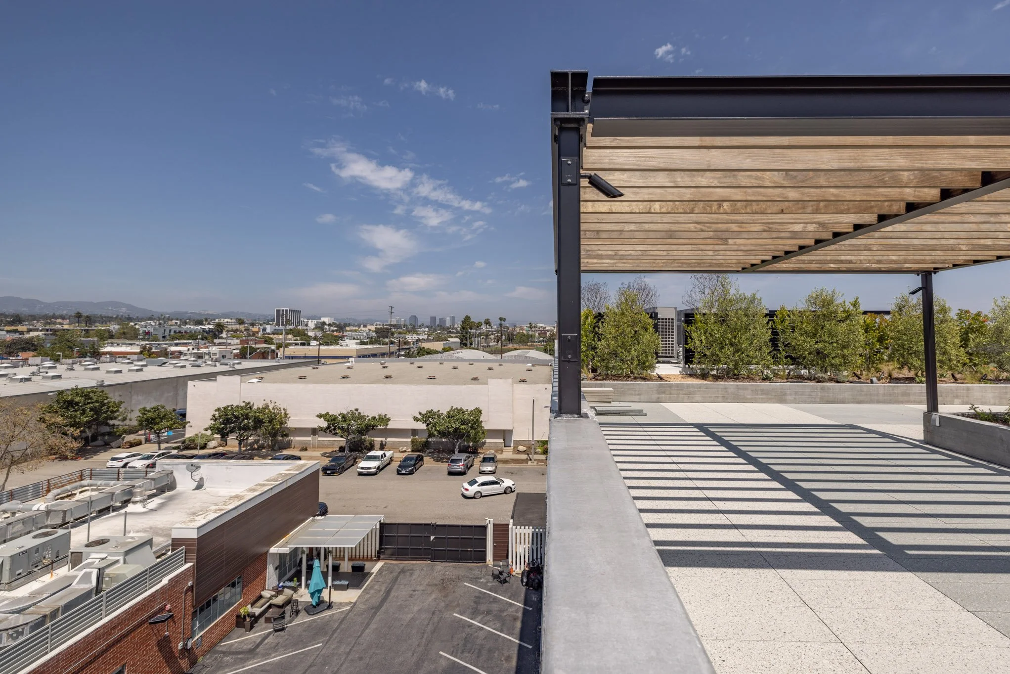 View from a rooftop terrace showing parking lot, trees, and distant city skyline under cloudy sky