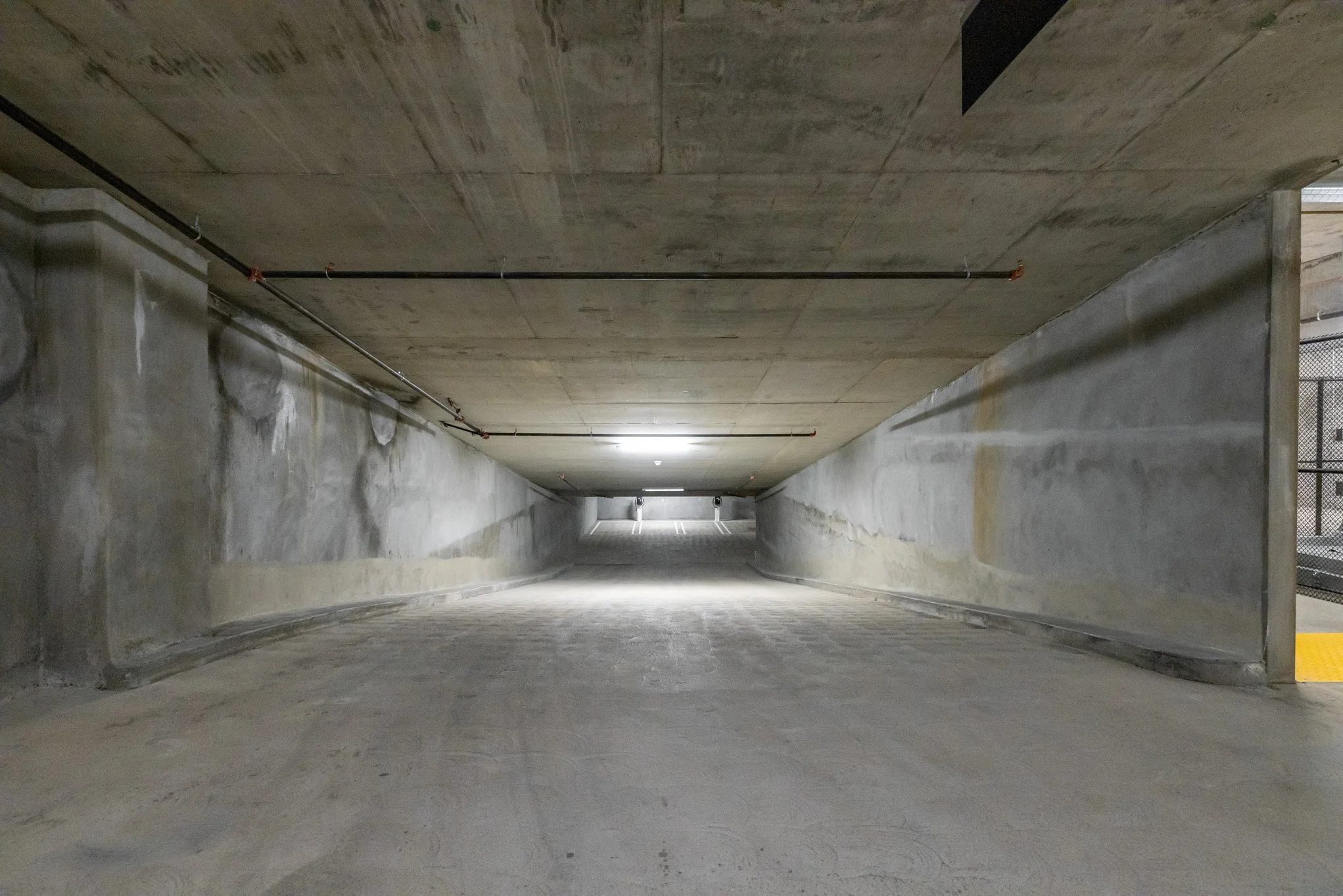 Underground parking garage ramp with concrete walls and ceiling, illuminated by overhead lights.