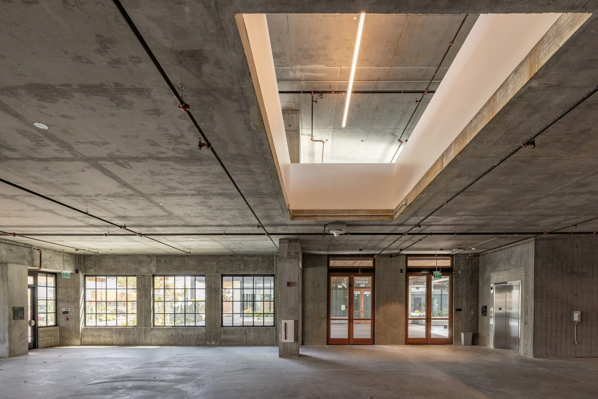 Empty commercial space with concrete walls, large windows, and a rectangular skylight in the ceiling.