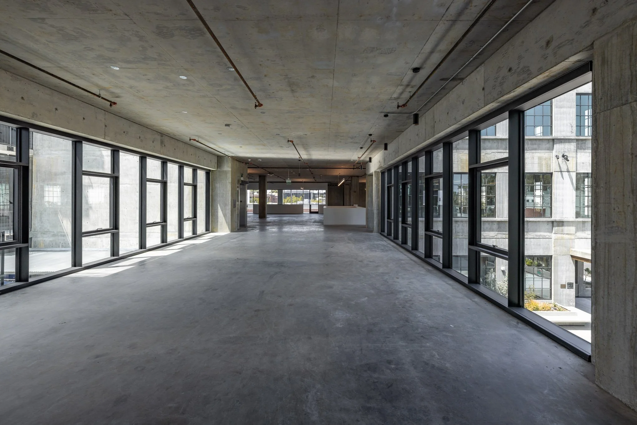 Empty modern commercial space with large windows, concrete floors, and unfinished ceiling.