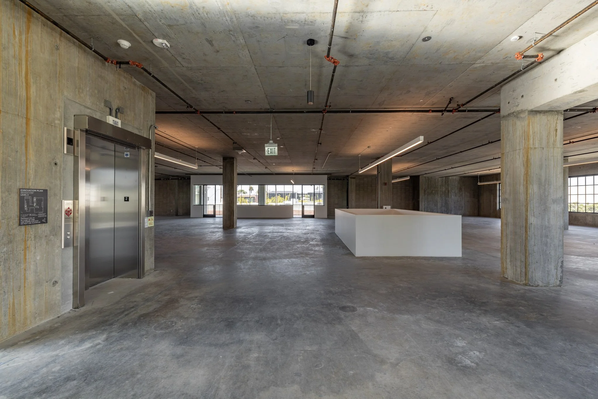 Empty multi-level parking garage with concrete pillars, an elevator, and large windows.