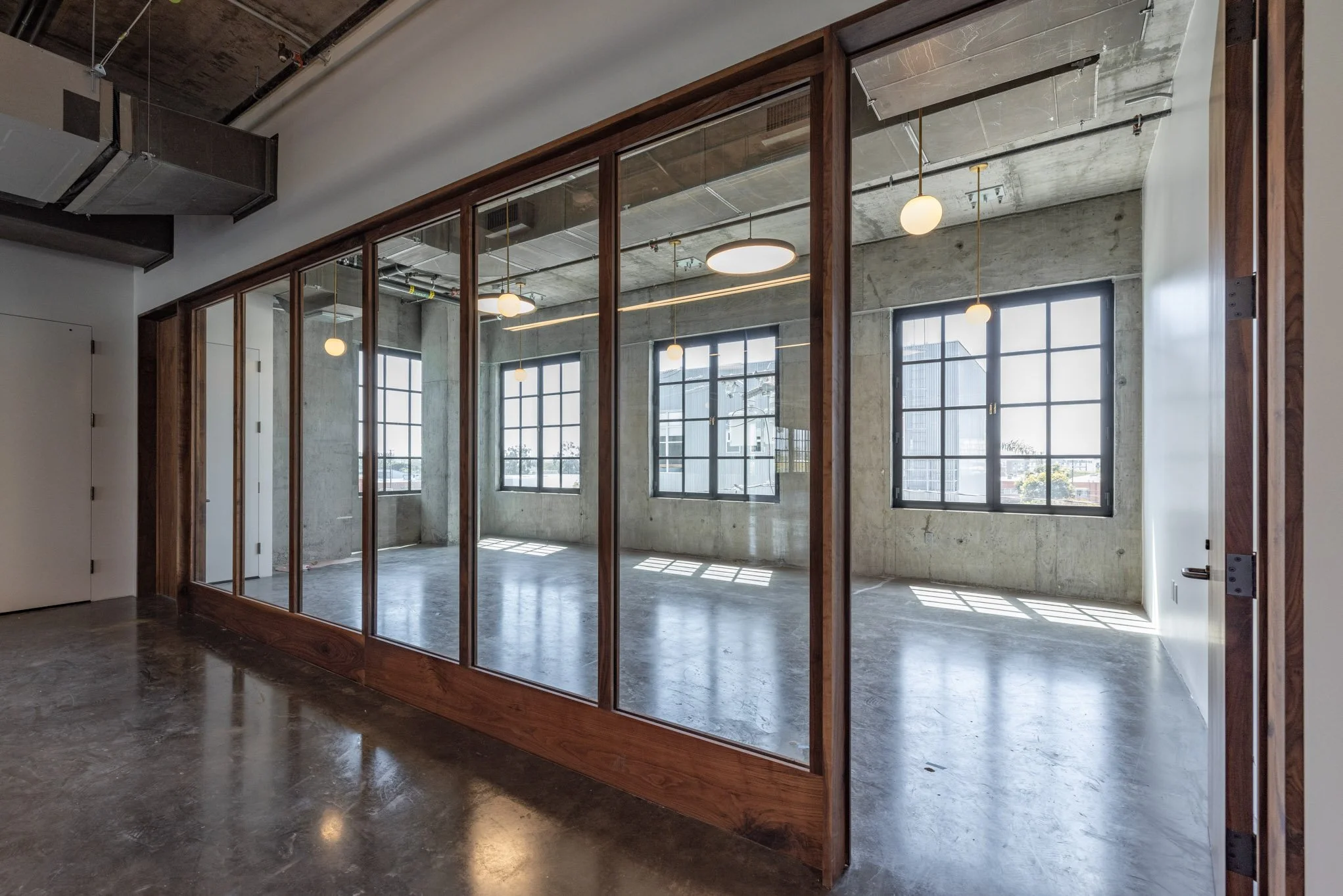 Empty modern office space with large windows, concrete walls, and a glass partition with wooden framing.