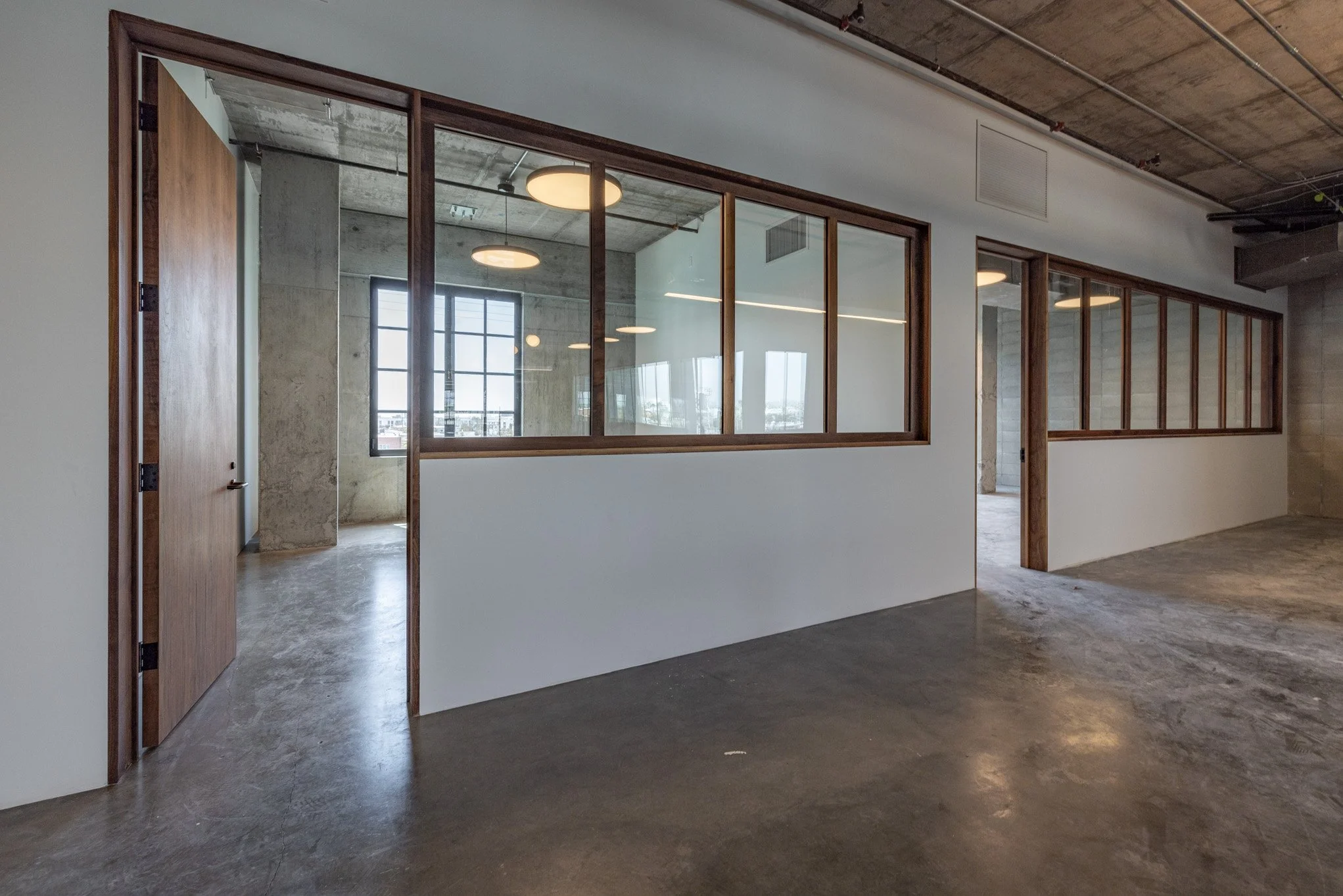 Empty office space with concrete floors, exposed ceilings, and glass-walled rooms.