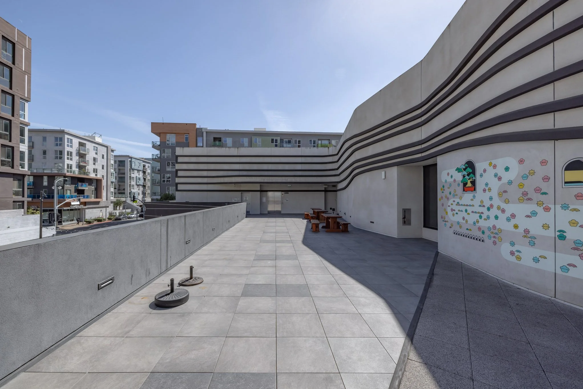 Empty outdoor terrace with benches, a colorful mural, and surrounding modern apartment buildings.