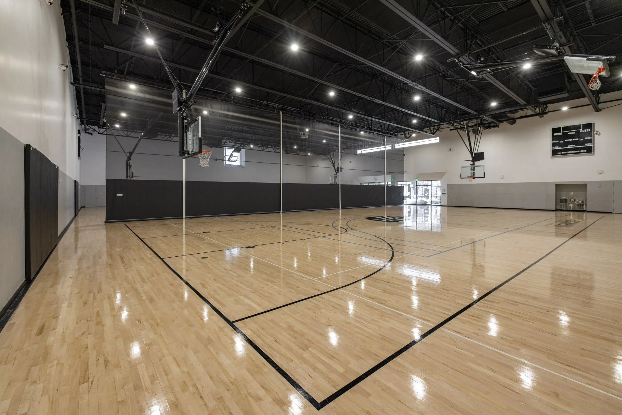 Empty indoor basketball court with polished wood flooring, basketball hoops, and scoreboard.