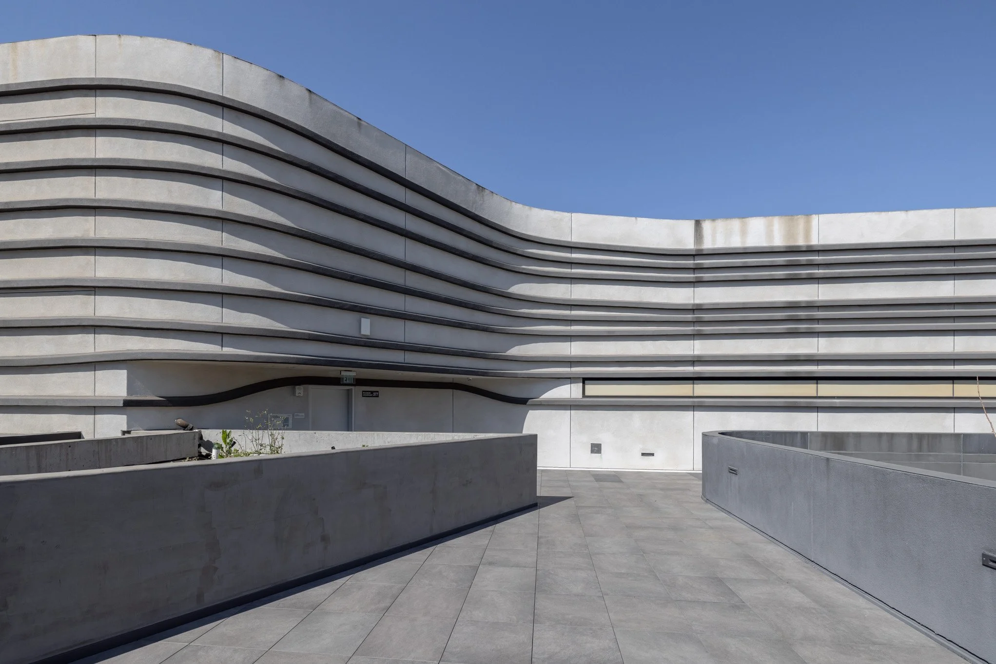 Modern concrete building with curved layered design and a clear blue sky.