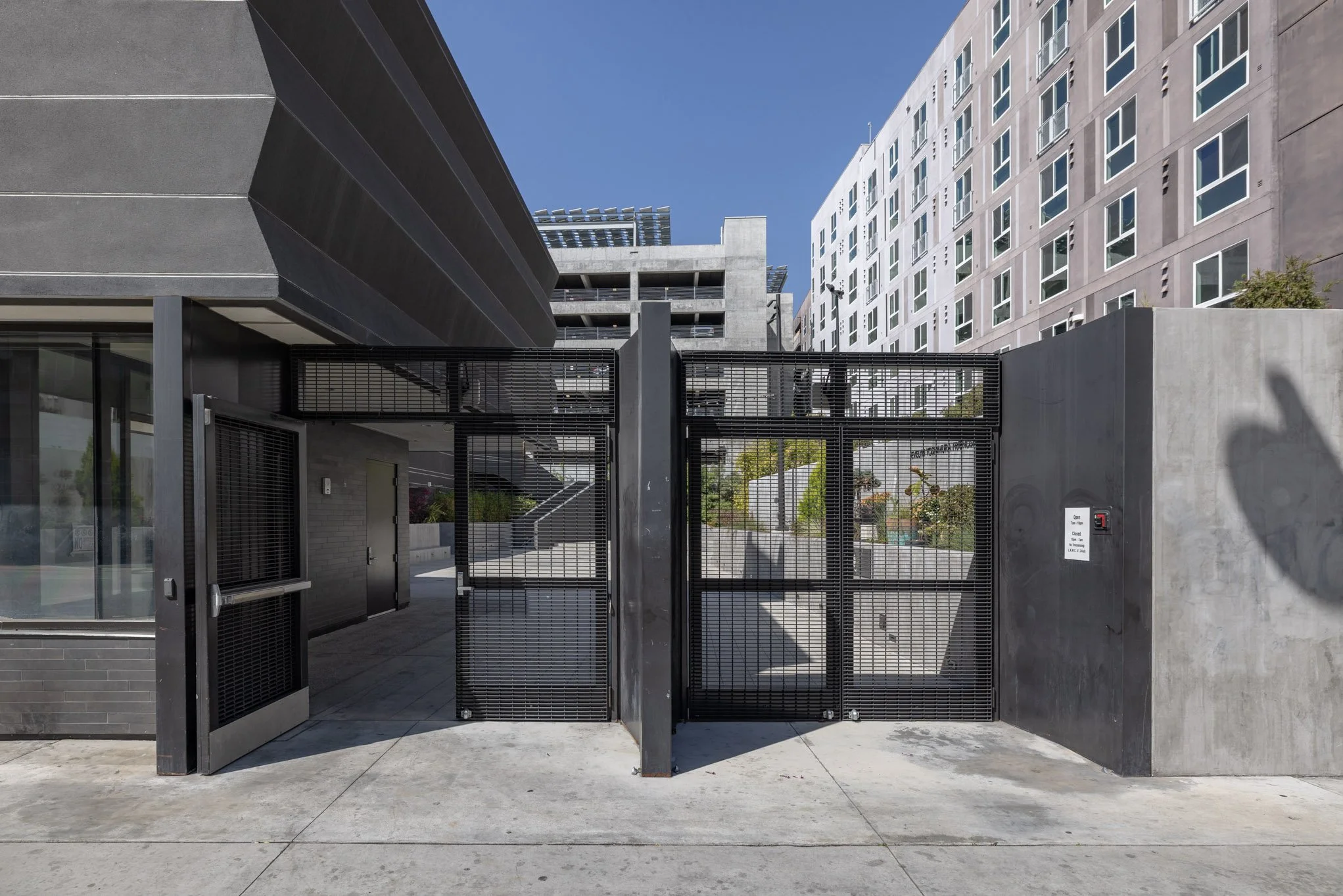 Secure gated entrance to a modern urban building with black metal gate and surrounding gray concrete and glass structures