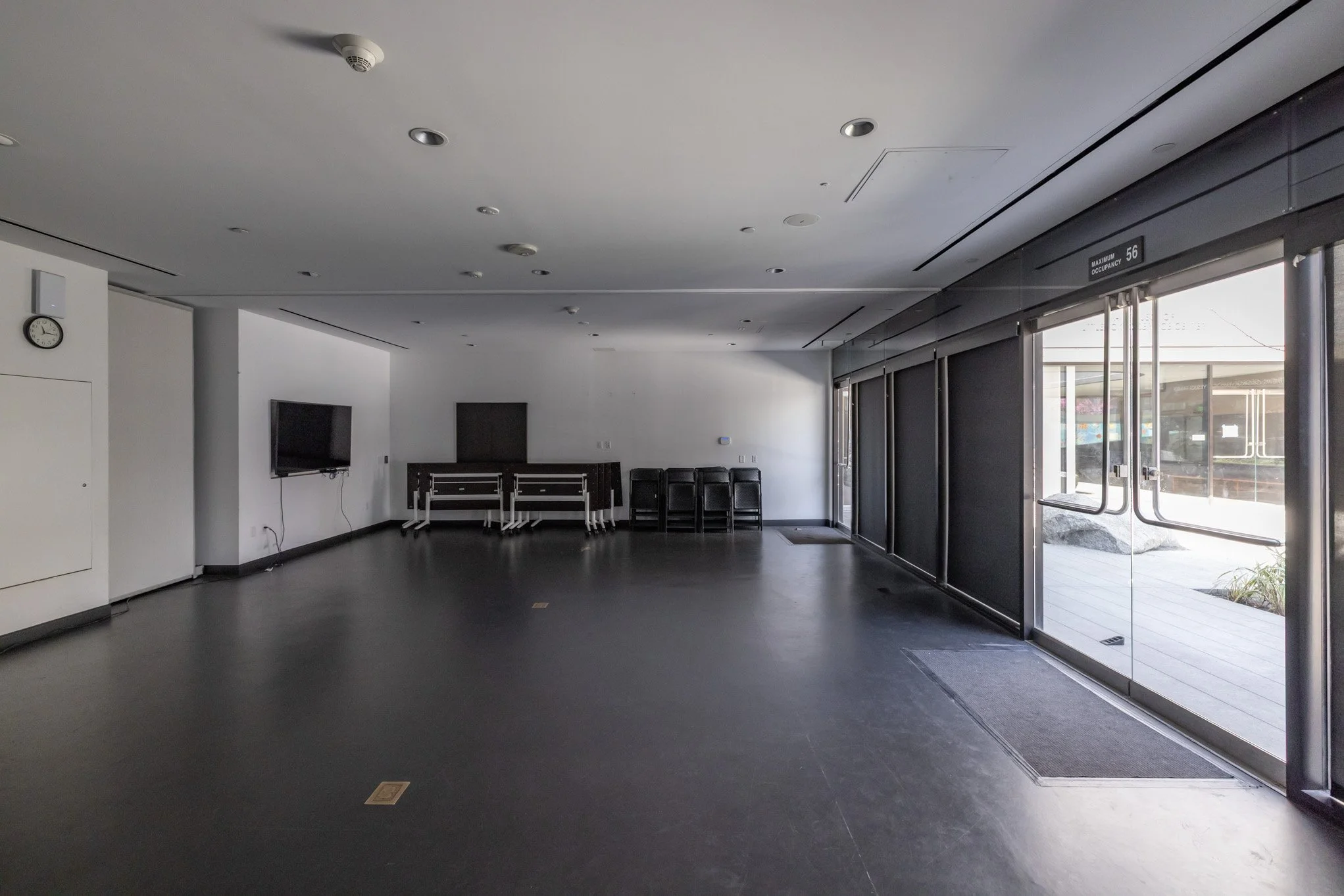 Empty room with chairs stacked against the wall, a television, and large glass doors leading outside.