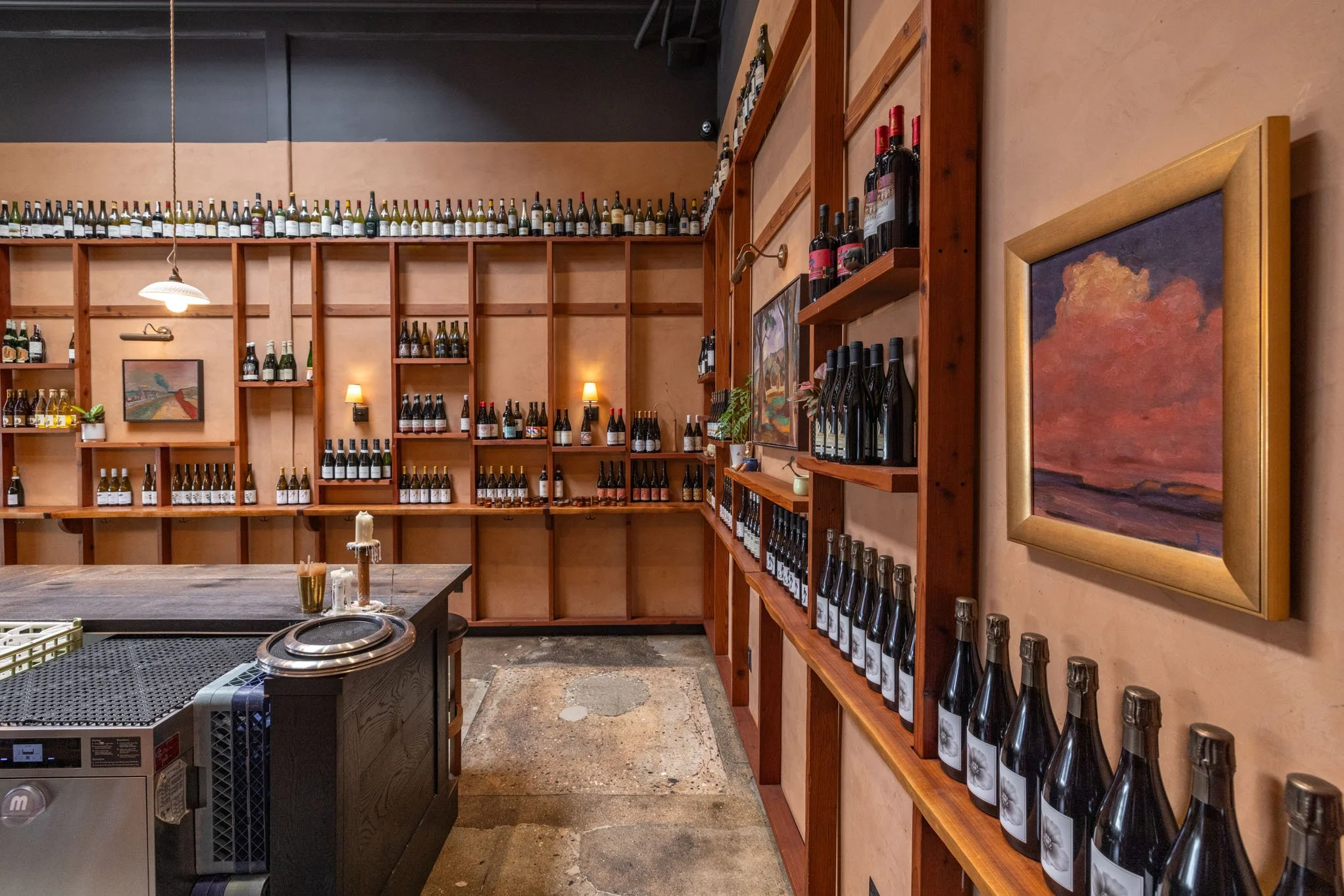 Interior of a wine shop showing wooden shelves filled with bottles of wine and paintings on the wall.