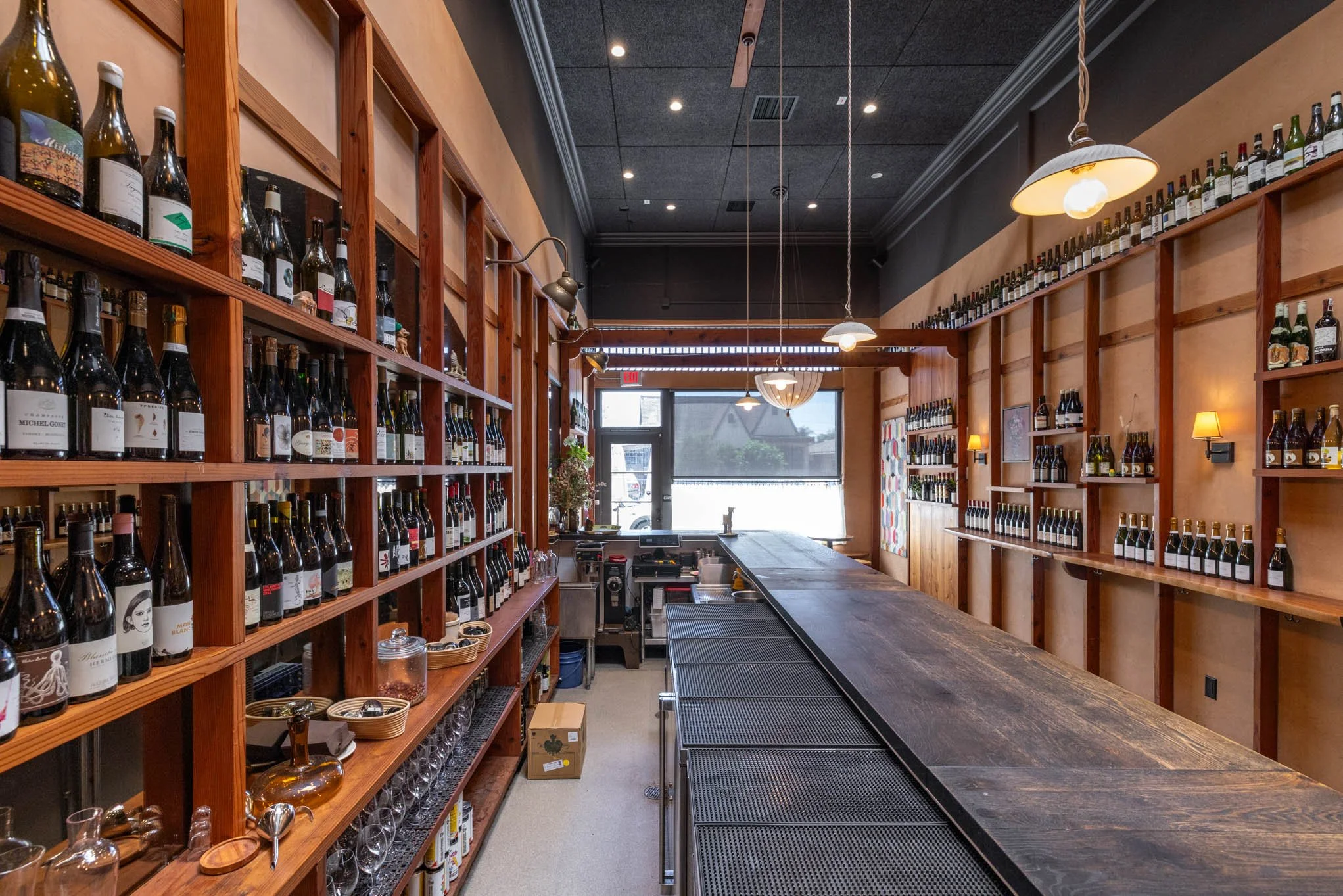 Interior of a wine shop or bar with wooden shelves stocked with bottles of wine, a wooden bar counter, and warm lighting.