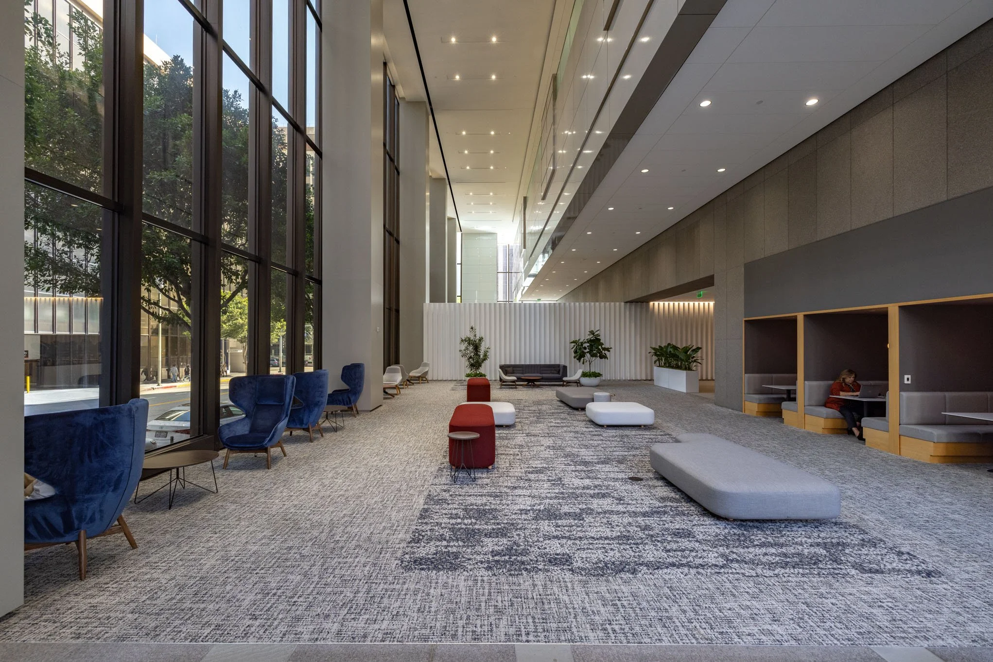 Modern lobby with large windows, blue chairs, gray benches, and potted plants.