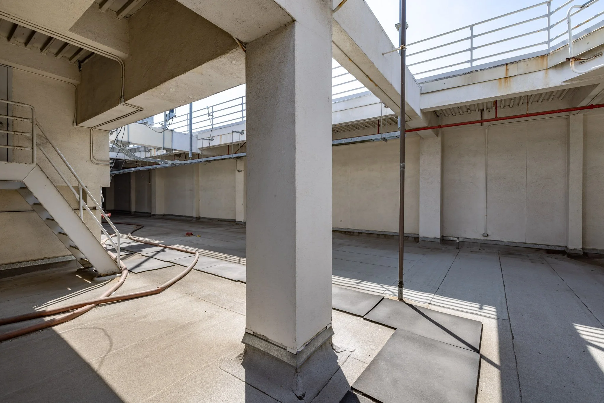 Concrete rooftop parking area under construction with pipes, support beams, and safety railing.