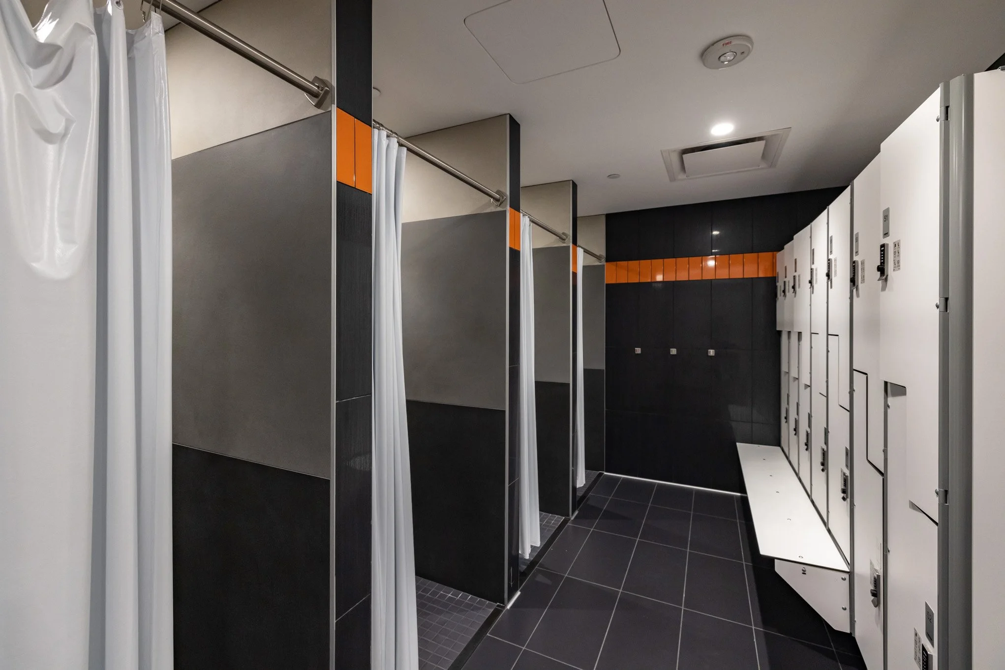Changing stalls with black and white lockers and white curtains in a modern gym or locker room.