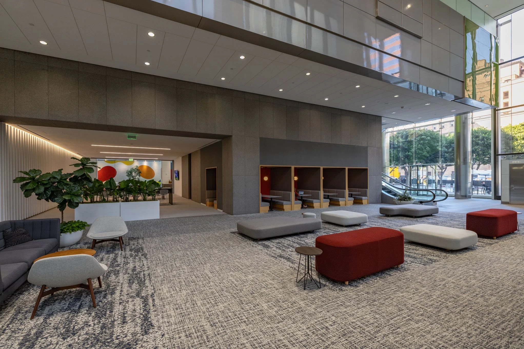 Modern hotel lobby with seating area, large windows, escalator, indoor plants, and abstract wall art.