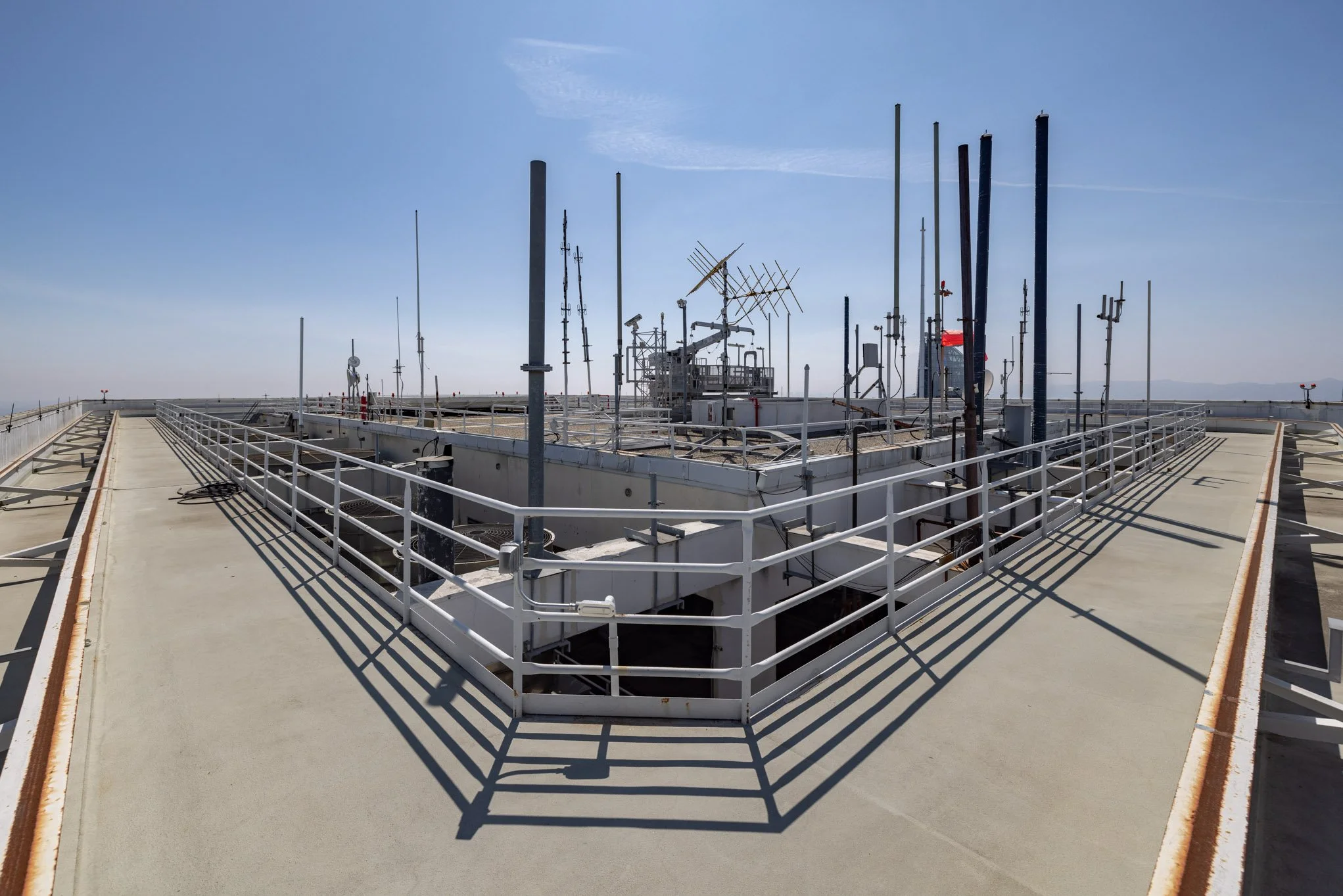 Rooftop of a building with communication antennas, satellite dishes, and metal poles under a clear blue sky.