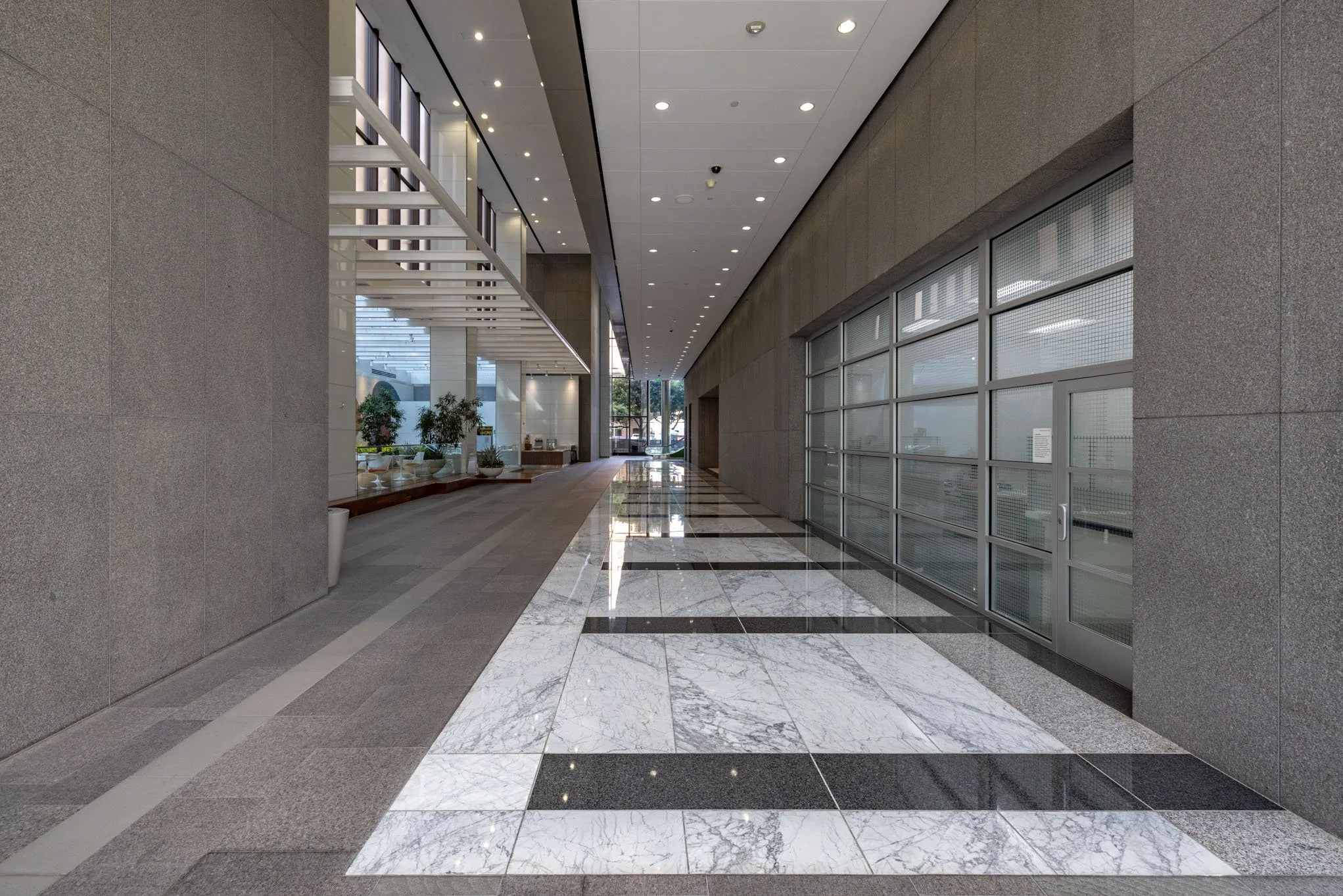Empty modern office lobby with marble floor, glass doors, and potted plants.