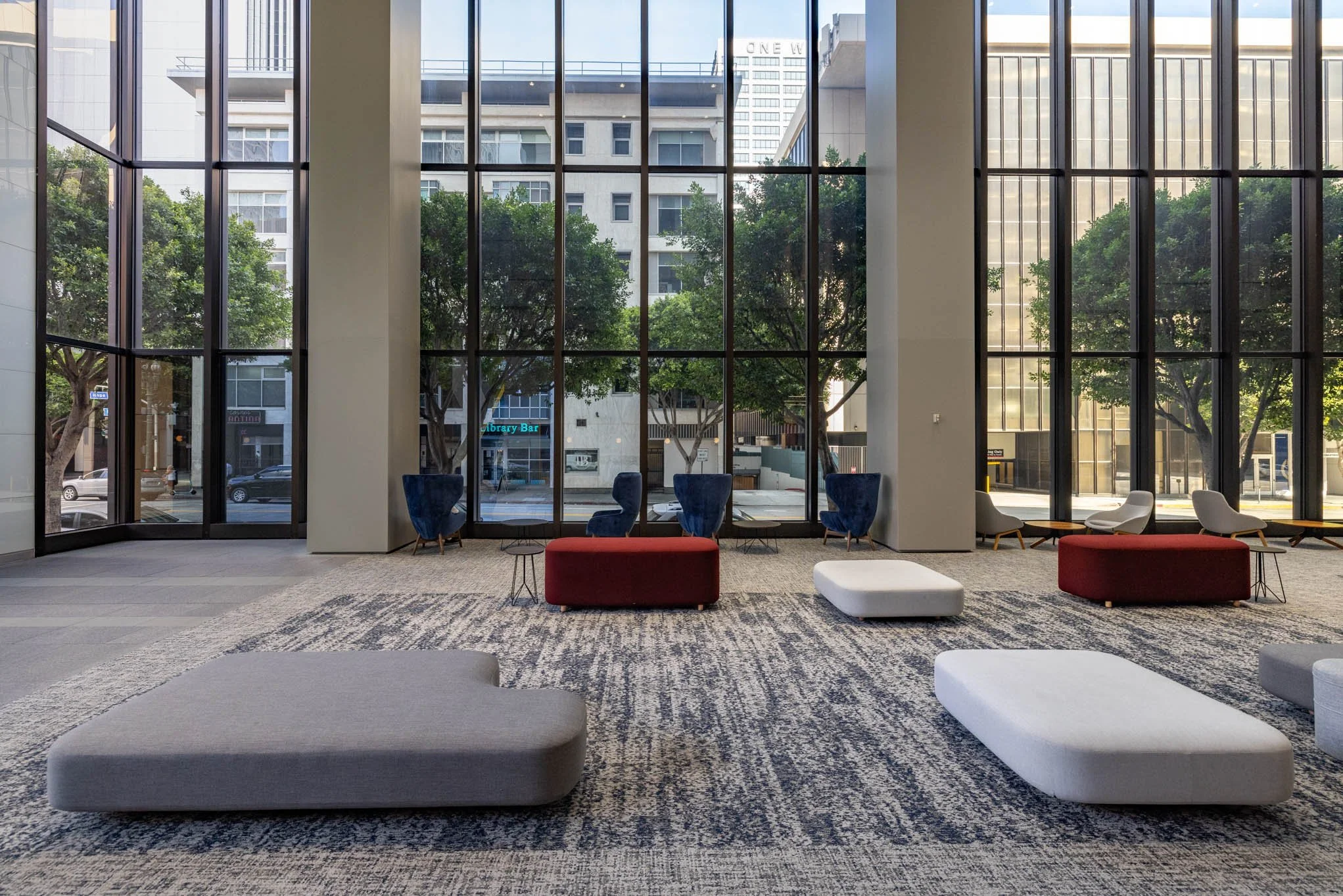 Modern hotel lobby with large glass windows, contemporary lounge chairs, and ottomans, overlooking city streets.